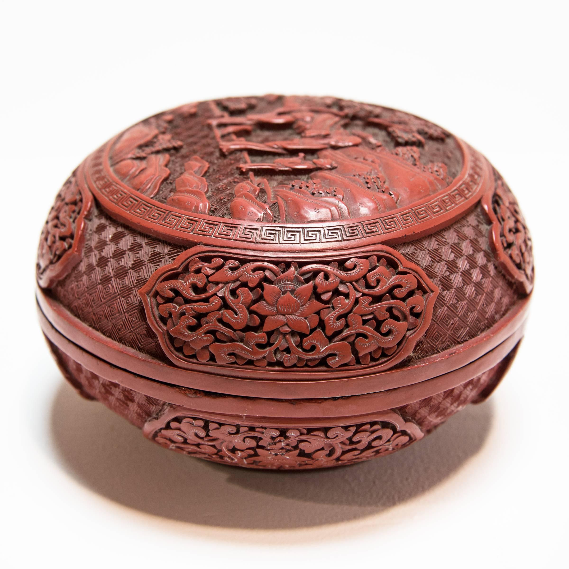 A mineral called cinnabar gives this domed box a stunning red color, and creates a striking contrast with the glossy, black interior. The entire surface is intricately carved: on the lid, three figures stroll through an idyllic garden setting; on