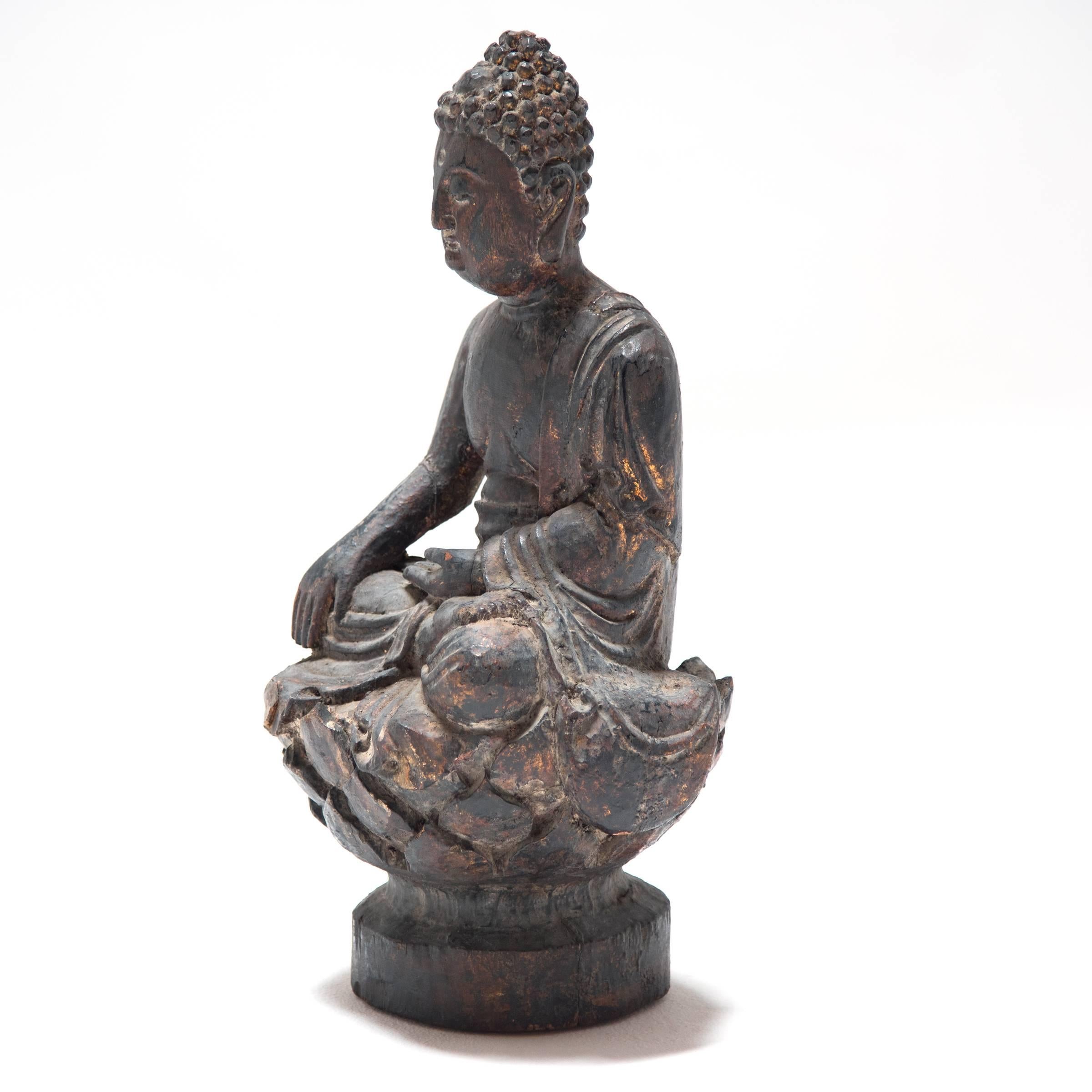 The flowing, draped robes that dress this serene depiction of the enlightened Buddha, Sakyamuni, are intricately carved. Traces of the the original lacquer are on the sole of his poised foot which is folded peacefully atop the sculpted lotus flower