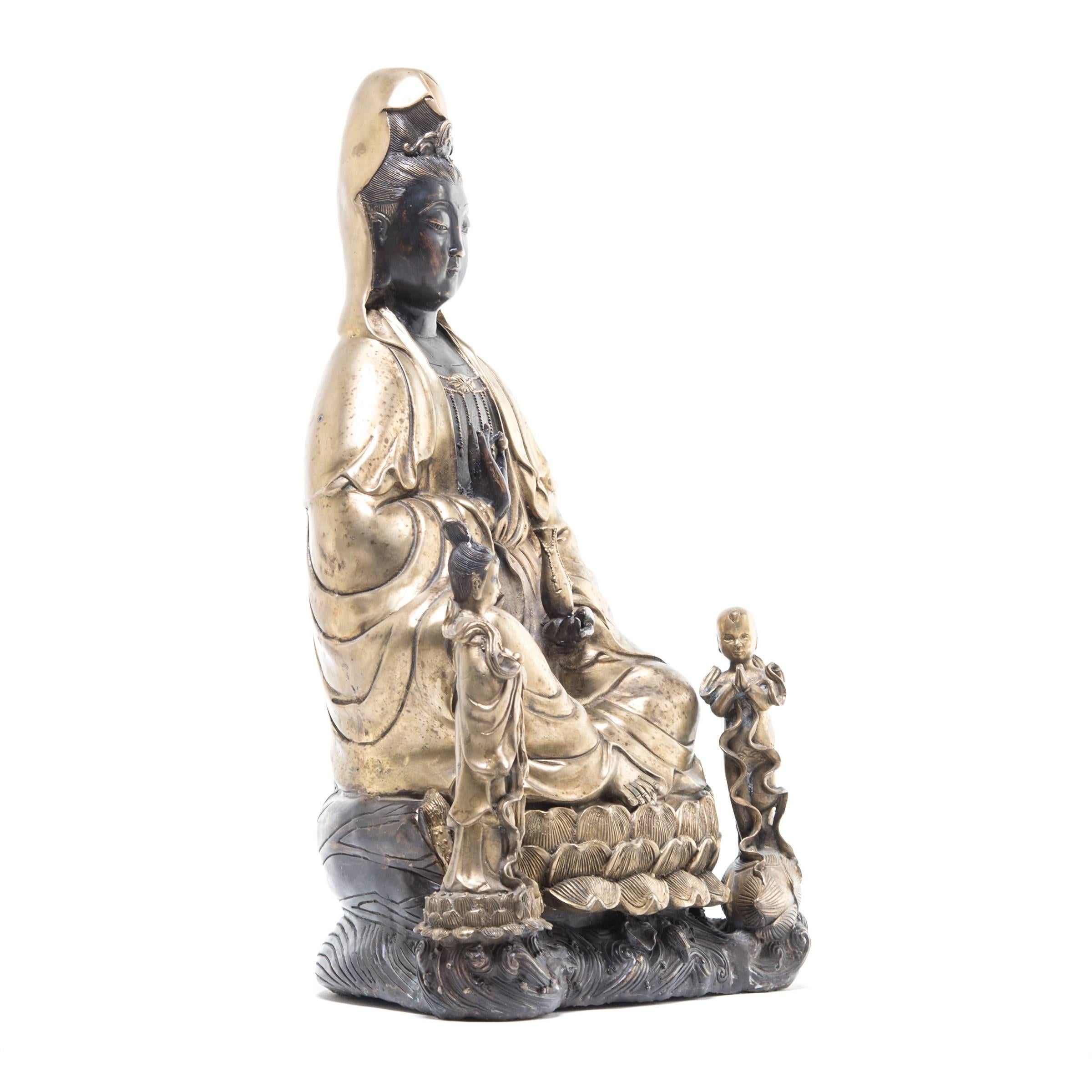 This majestic statue is a portrayal of Guan Yin, an enlightened bodhisattva of infinite compassion well known among East Asian Buddhists. She wears a serene expression and is seated on an exquisitely detailed lotus blossom throne with her attendants