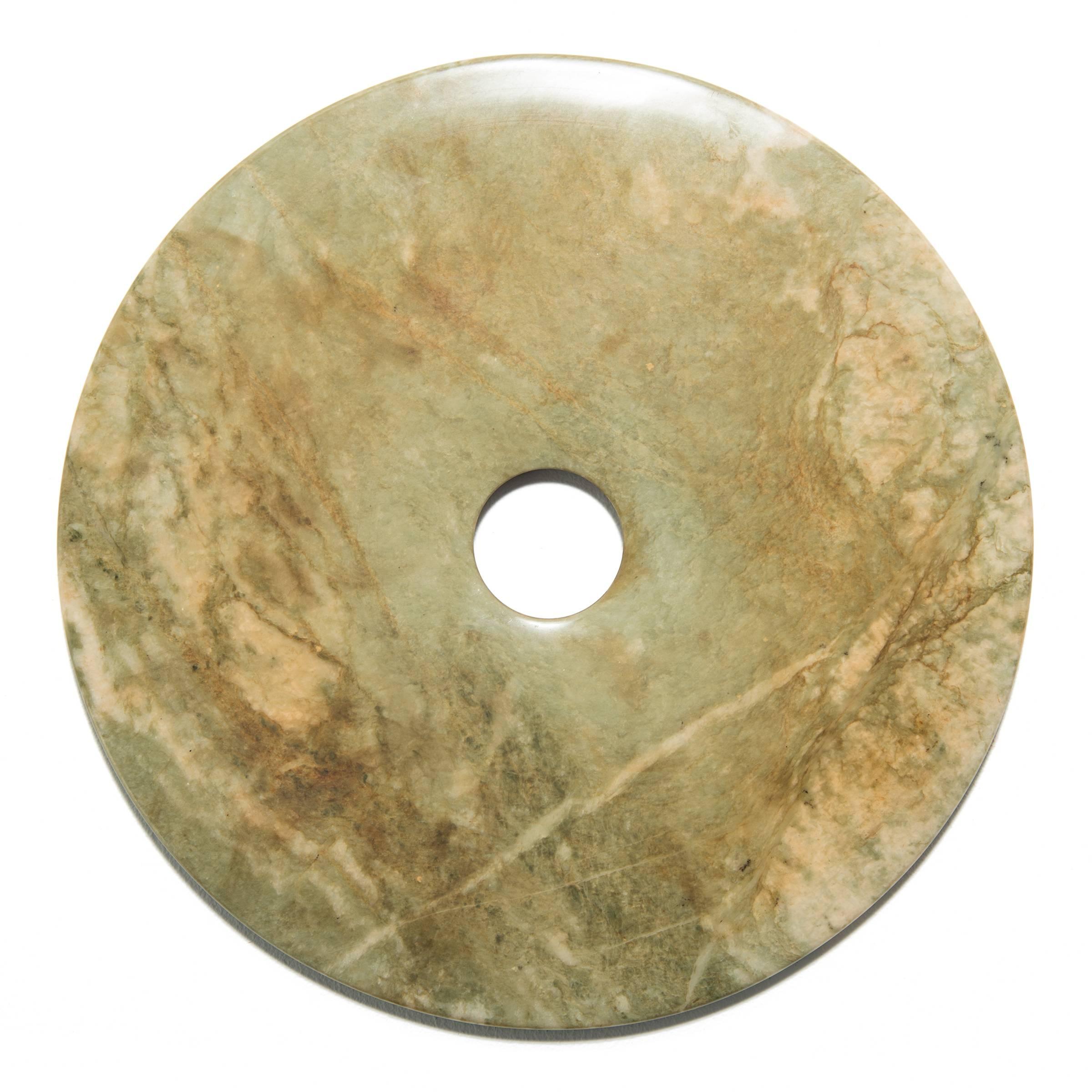 This mottled green and white disc is particularly striking in its custom mount. Shaping this hard stone takes considerable skill. An artisan imbues the jade with this soft, satiny glow by patiently rubbing the surface with sand, a subtle beauty