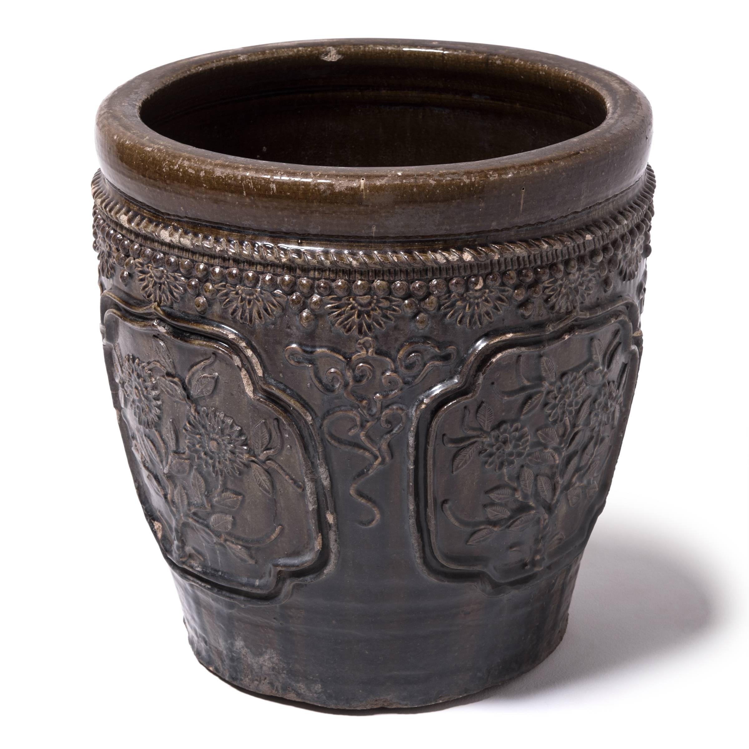 This large glazed jar was handcrafted in Shanxi province over a century ago. Masterfully crafted, the jar is patterned in high relief featuring medallions portraits of blooming flowers and trimmed around the rim with floral, bead and rope-like