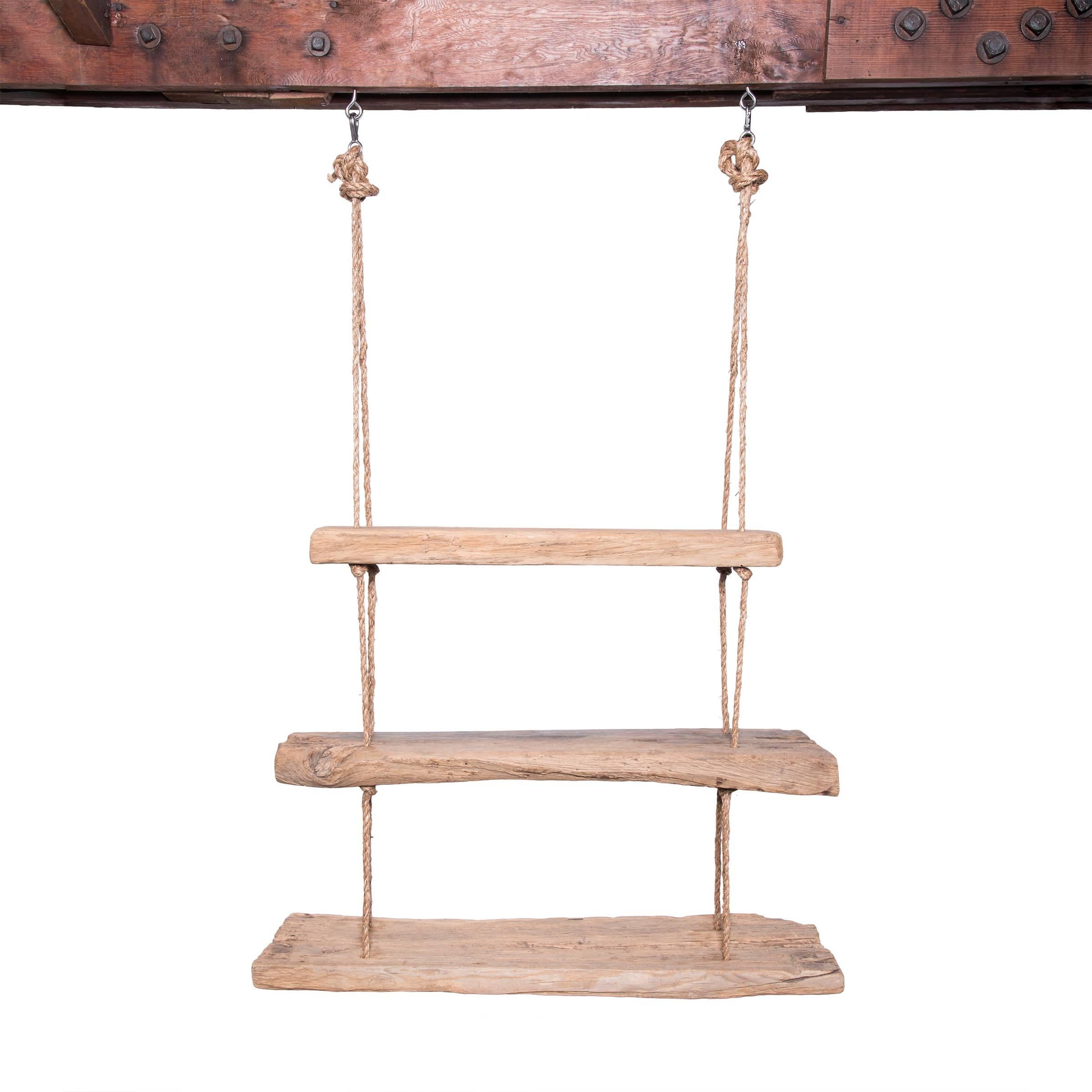 Timbers of reclaimed wood find new purpose as a suspended shelf. Tiered together with thick hemp rope, the rustic shelves are rich with character developed over time. Sturdy enough to support books or decorative objects, the shelves could also serve