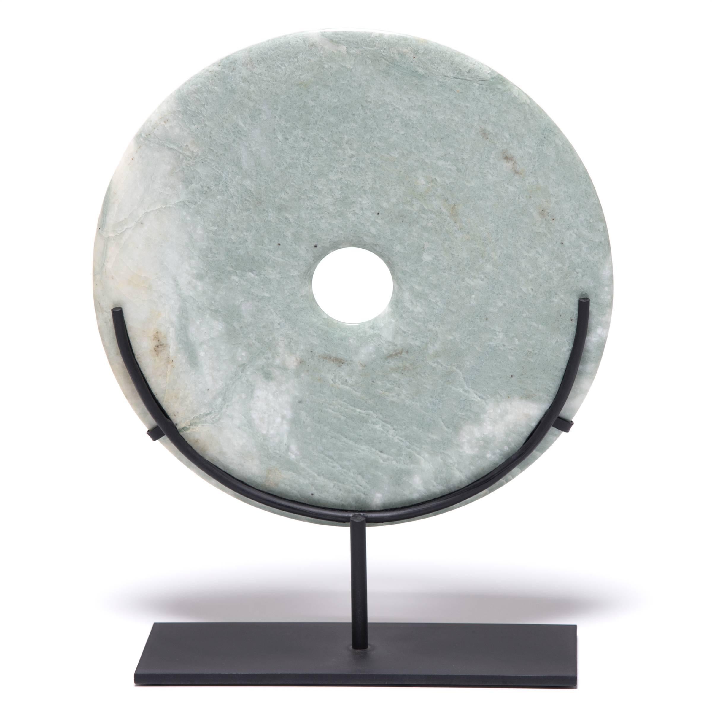 The creamy green color and natural variegation of this jade disk calls to mind a full moon on a dark night. Known as “bi,” these perfectly round discs with a circular hole in the centre originally date from Neolithic times. This contemporary example