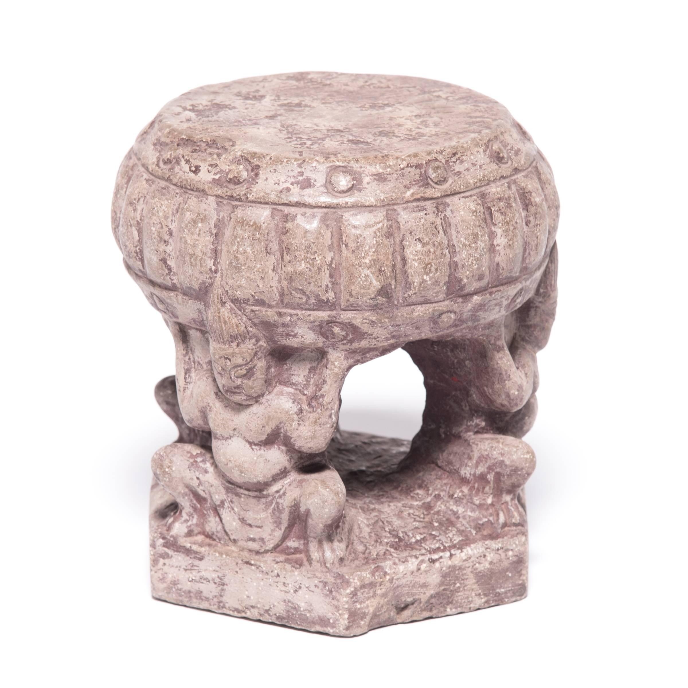 Probably paired up as architectural elements of a grand, Qing-dynasty Chinese home, this set of stone charms depicts a ring of squatting attendants hoisting a large drum. Symbols of power and wealth, the drums may have at one time been painted red