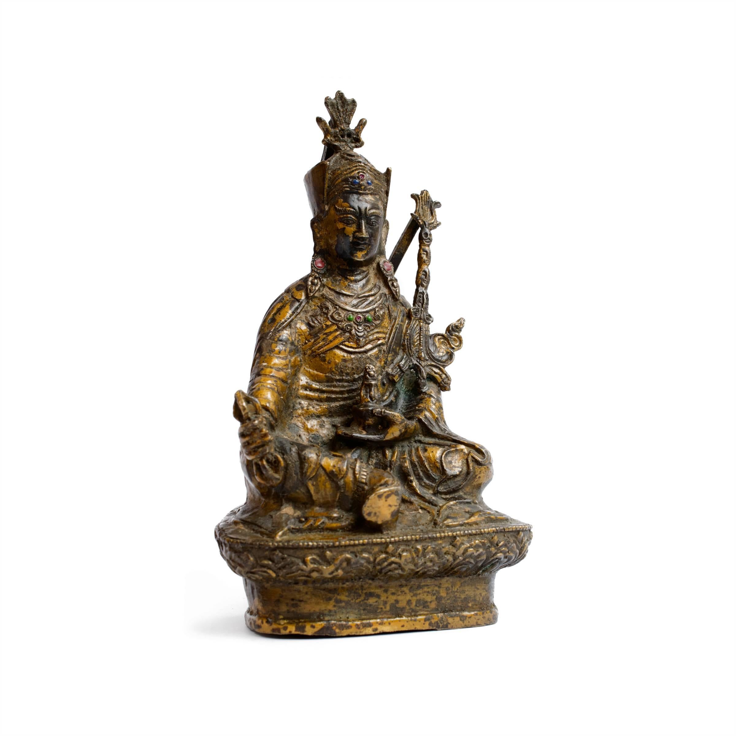 This Tibetan Buddhist deity is finely crafted out of gilded bronze and inlaid with stones. The figure holds a bottle in his left hand and in his right a varja—a powerful ritual object symbolizing indestructibility and irresistible force—he is seated