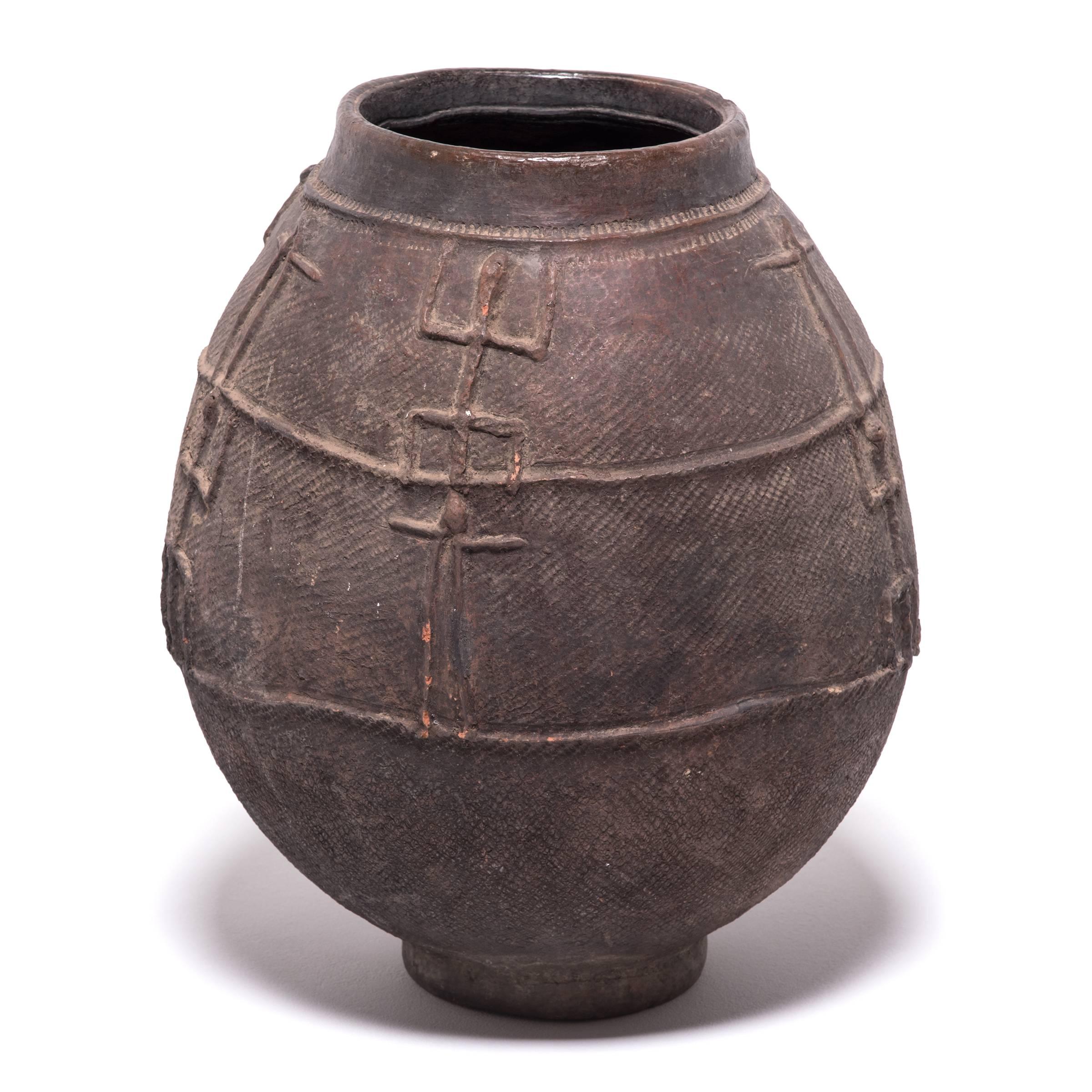 Formed by pounding flattened clay around a convex mold, this oblong footed vessel is a water storage jar known as a jidaga, created by women of the Bambara people of Mali. The body of the wide-mouth jar is patterned with abstract figures of humans