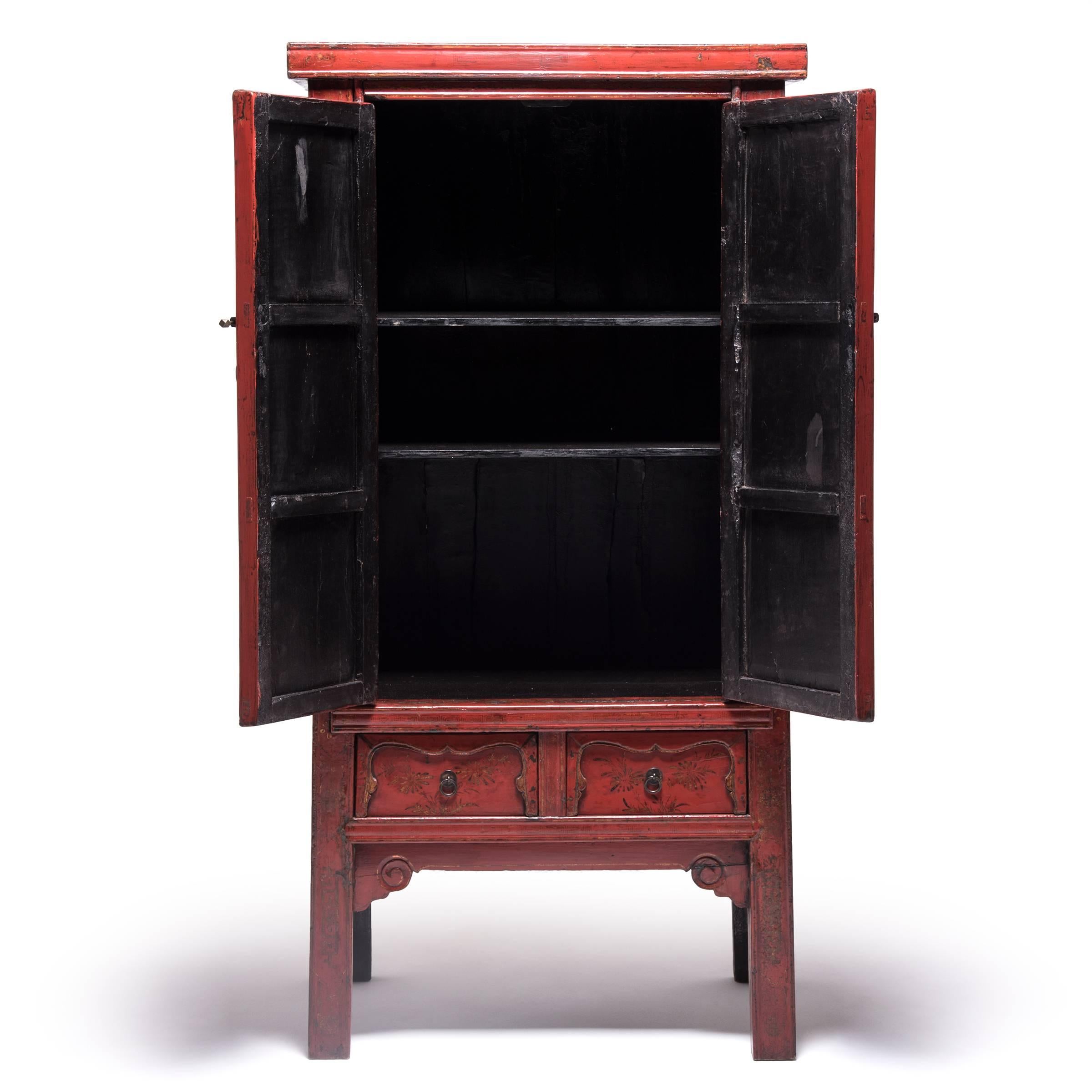 The lyrical lines and brilliant red lacquer of this stately 19th century cabinet must have proved irresistible to the artisan who painted its surfaces with intricate detail. Long, vertical doors provided the perfect canvas for a pair of