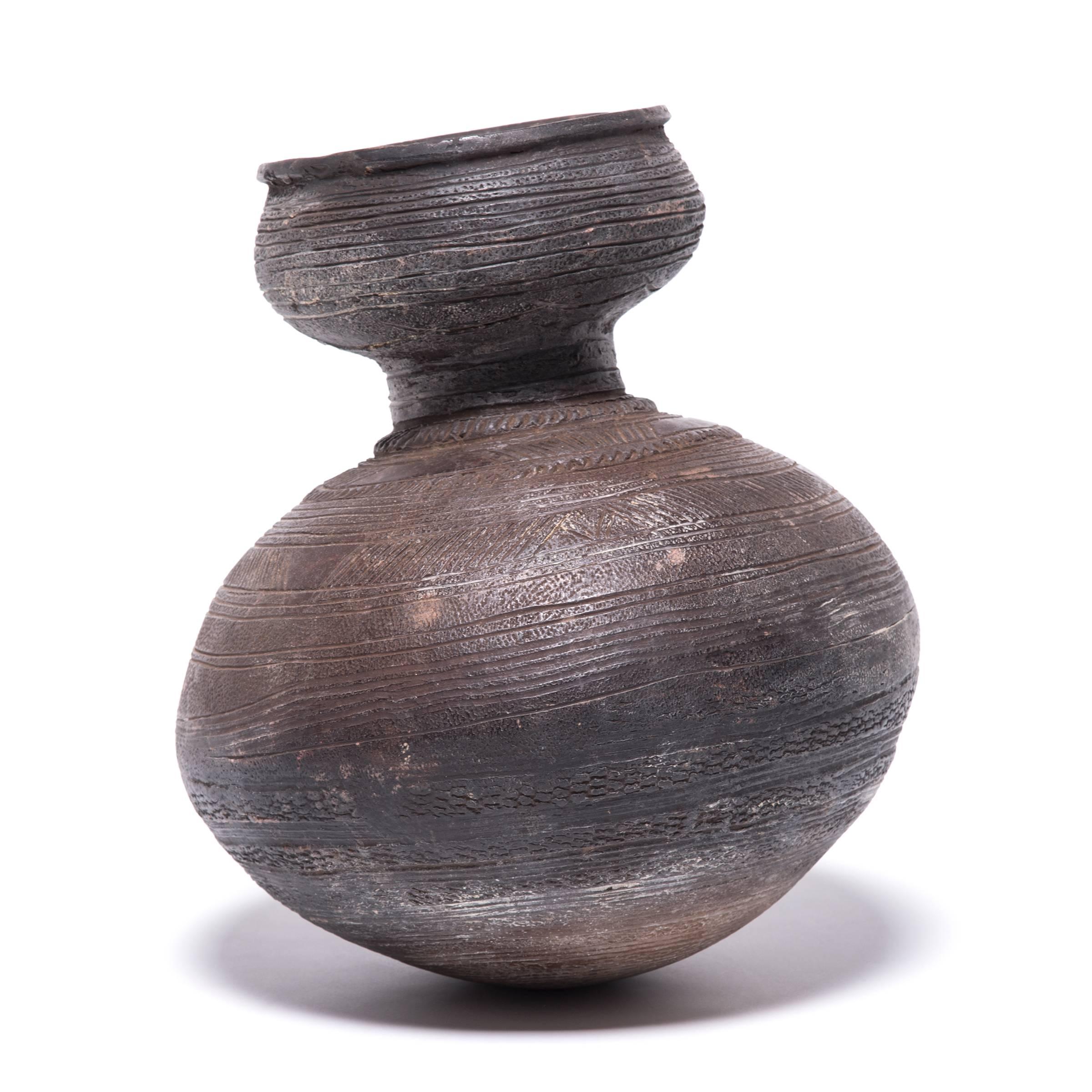 Inspired by the natural world, nupe ceramicists fired this water vessel in the shape of a gourd. The vessel's varied textures and colors come from its utilitarian design. The parallel banding and arched motifs create a handworn texture that