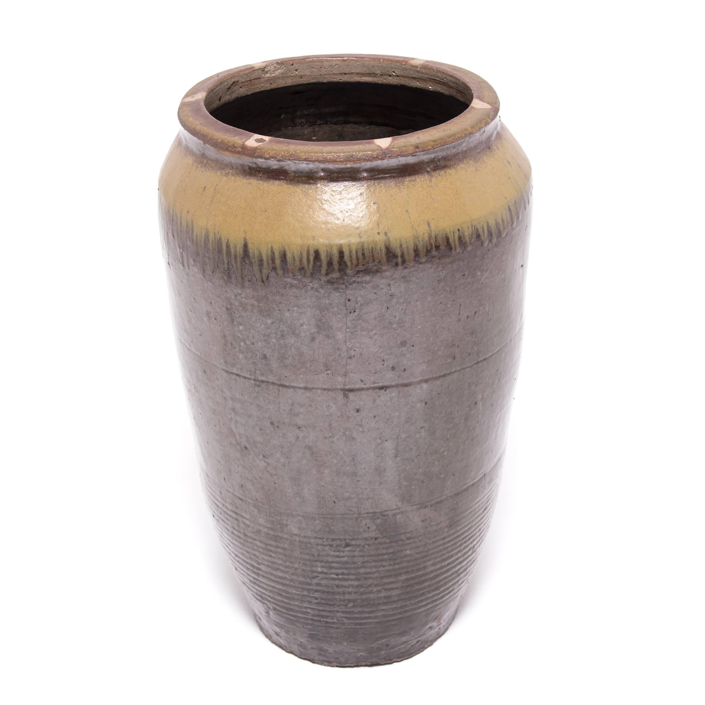 Used to store wine or other spirits, this tall jar dates from 1900. Choosing a simple shape, the potter shows off his talent in the beautiful glazing technique. A thin base glaze warms the surface while allowing the ripples of its spun manufacture