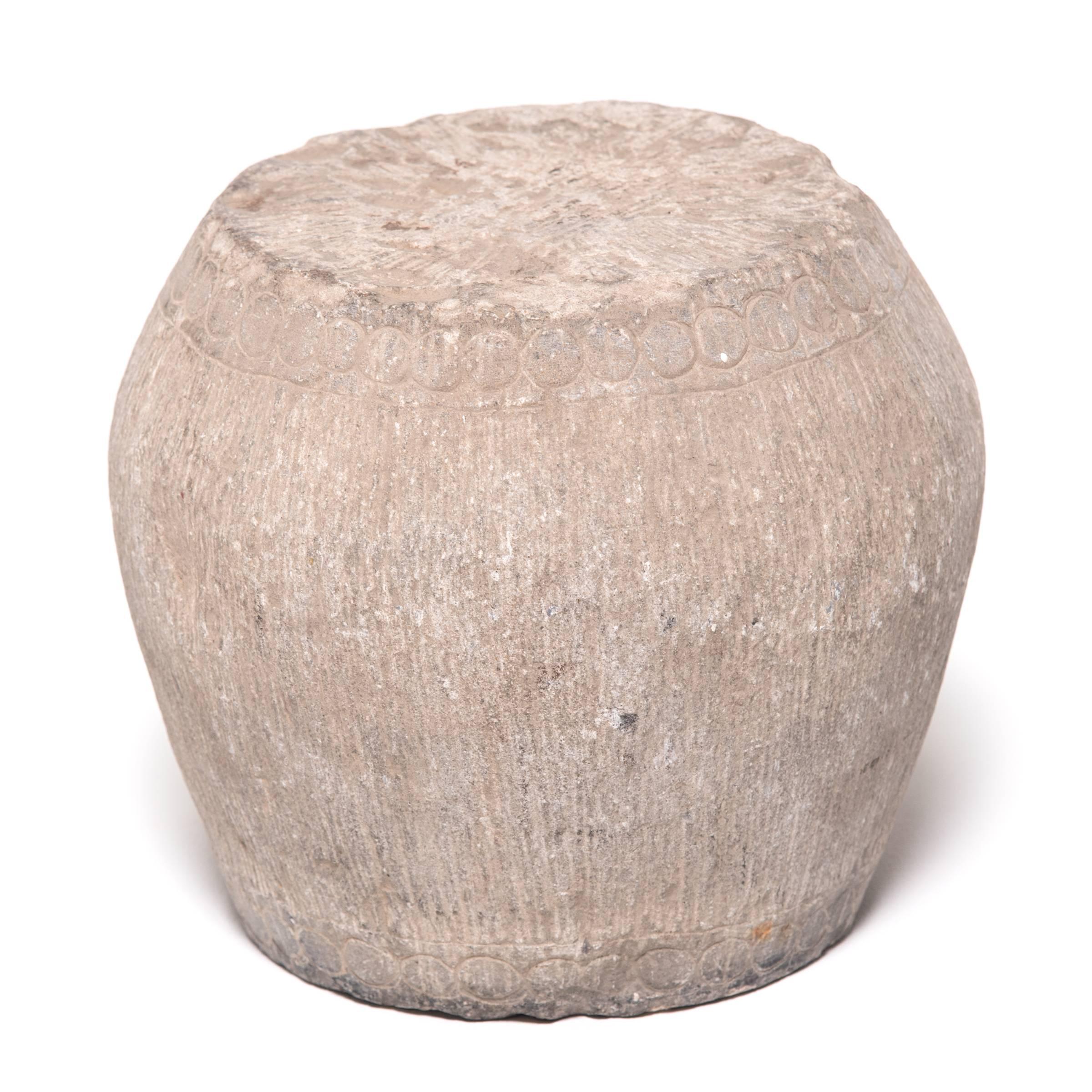 Look closely and you can just make out the hand-carved details that once made this small stone stool resemble a drum. A ring of circles along the top and bottom imitates bosshead nails used to stretch a skin on an actual drum, and thin vertical