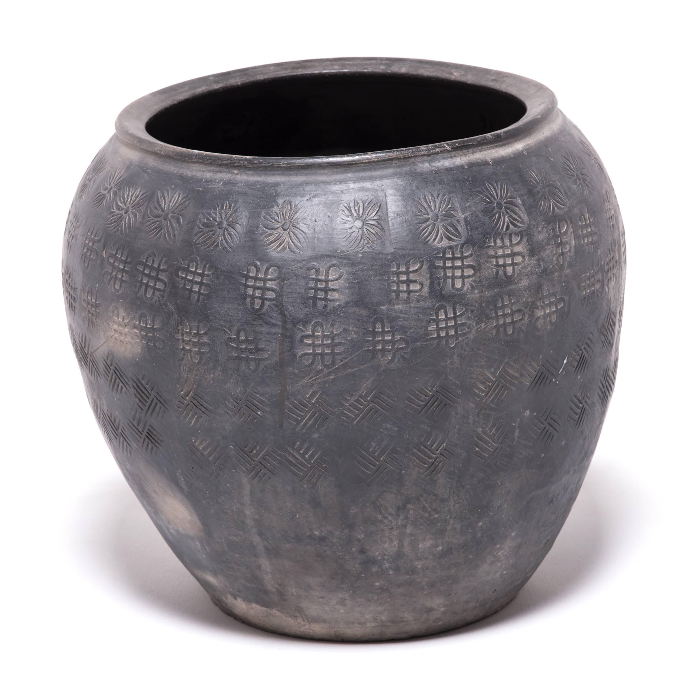 Over a century ago, a gifted potter from northern China crafted this organic clay jar out of rich dark river clay mined from the river basins of Asia. The surface is stamped with auspicious symbols: The Tibetan Buddhist endless knot, and the peony,