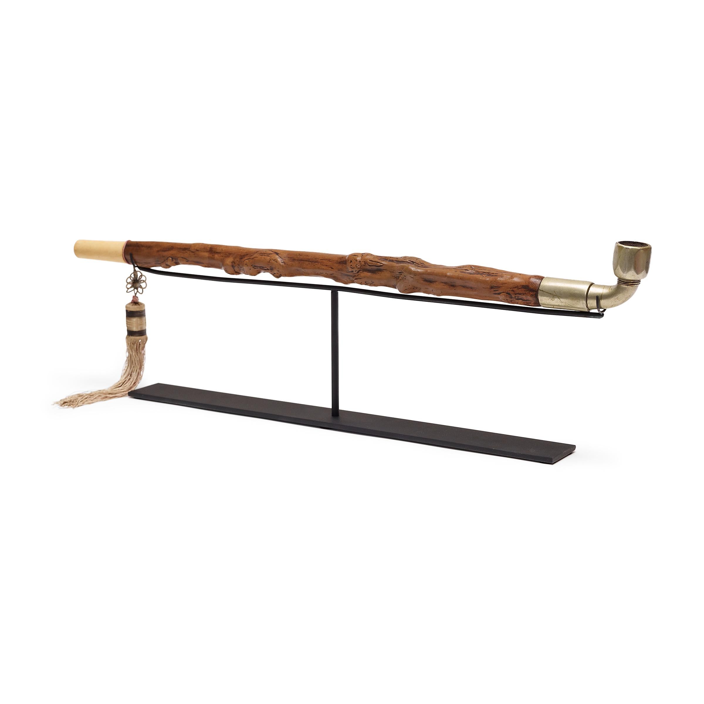 Questa monumentale pipa cinese è splendidamente scolpita con un lungo manico in legno di bosso che ricorda un ramo nodoso con nodi e bave. Sebbene le sue dimensioni imponenti ricordino le grandi pipe da oppio in bambù, la pipa del XIX secolo sarebbe