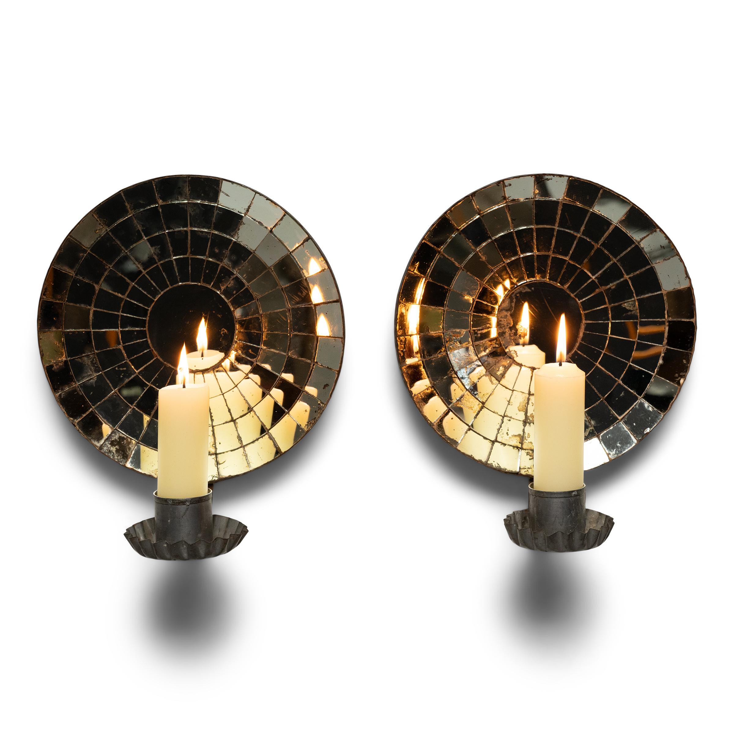 At once modern and traditional, these 1930s candle sconces are backed with circular mirrored reflectors, painstakingly assembled to a mosaic design from individual pieces of cut mirror glass. Marked with imperfections and spoiling from a century of