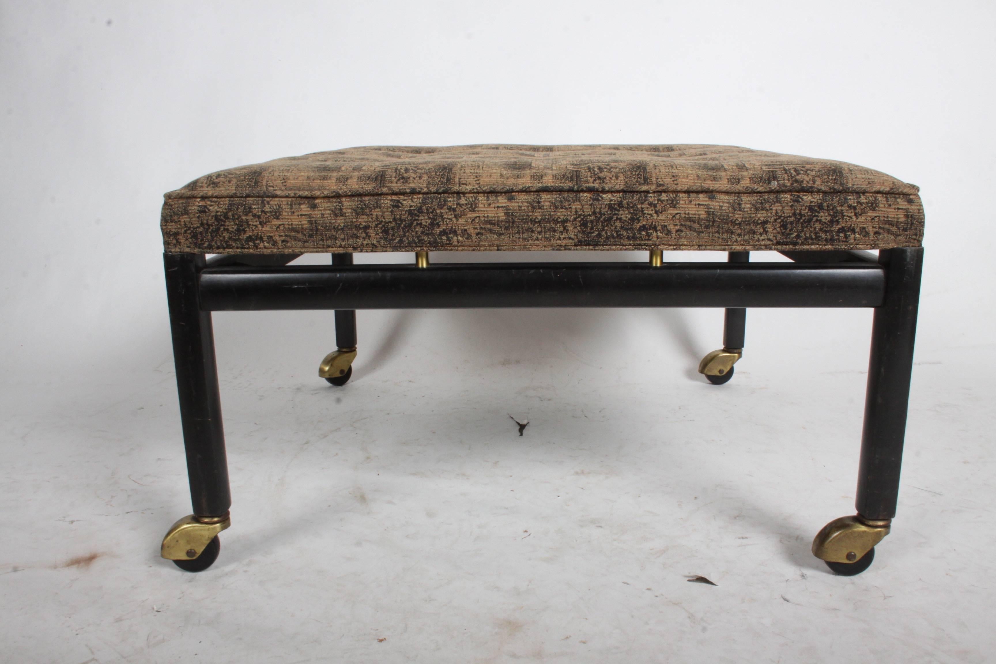 Vintage Michael Taylor for Baker Furniture Co. ottoman with brass castors. Original ebonized finish and upholstery, seat raised on brass cylinders. Label.