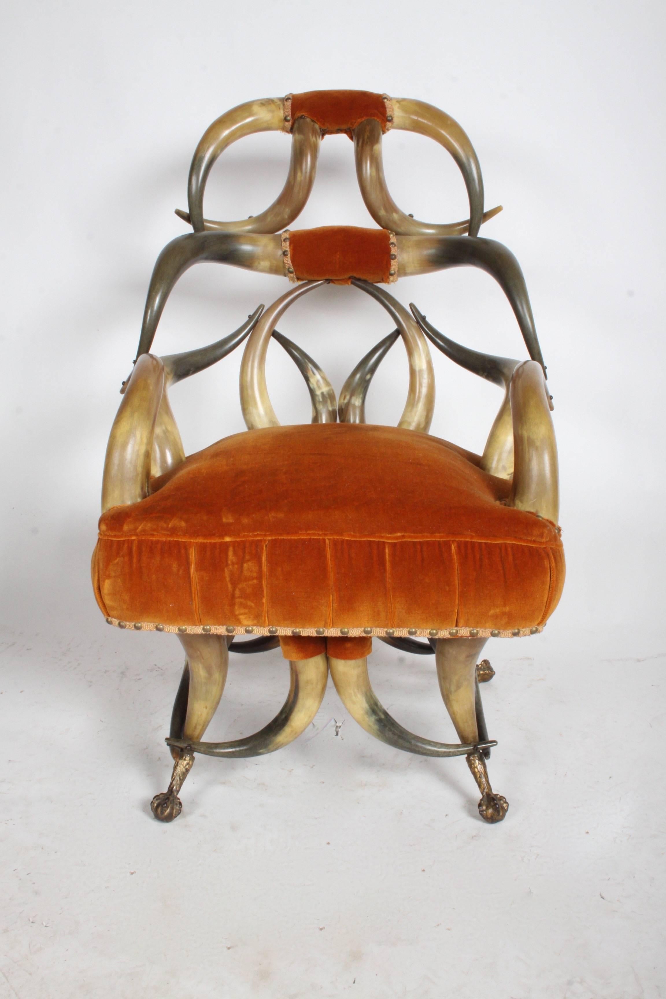 Incredible late 19th or early 20th century rustic steer long horn chair and ottoman. This chair is in great condition, has spring seat and is very sturdy. Older burnt orange velvet upholstery. Chair rest on gilded claw and ball feet. Ottoman has