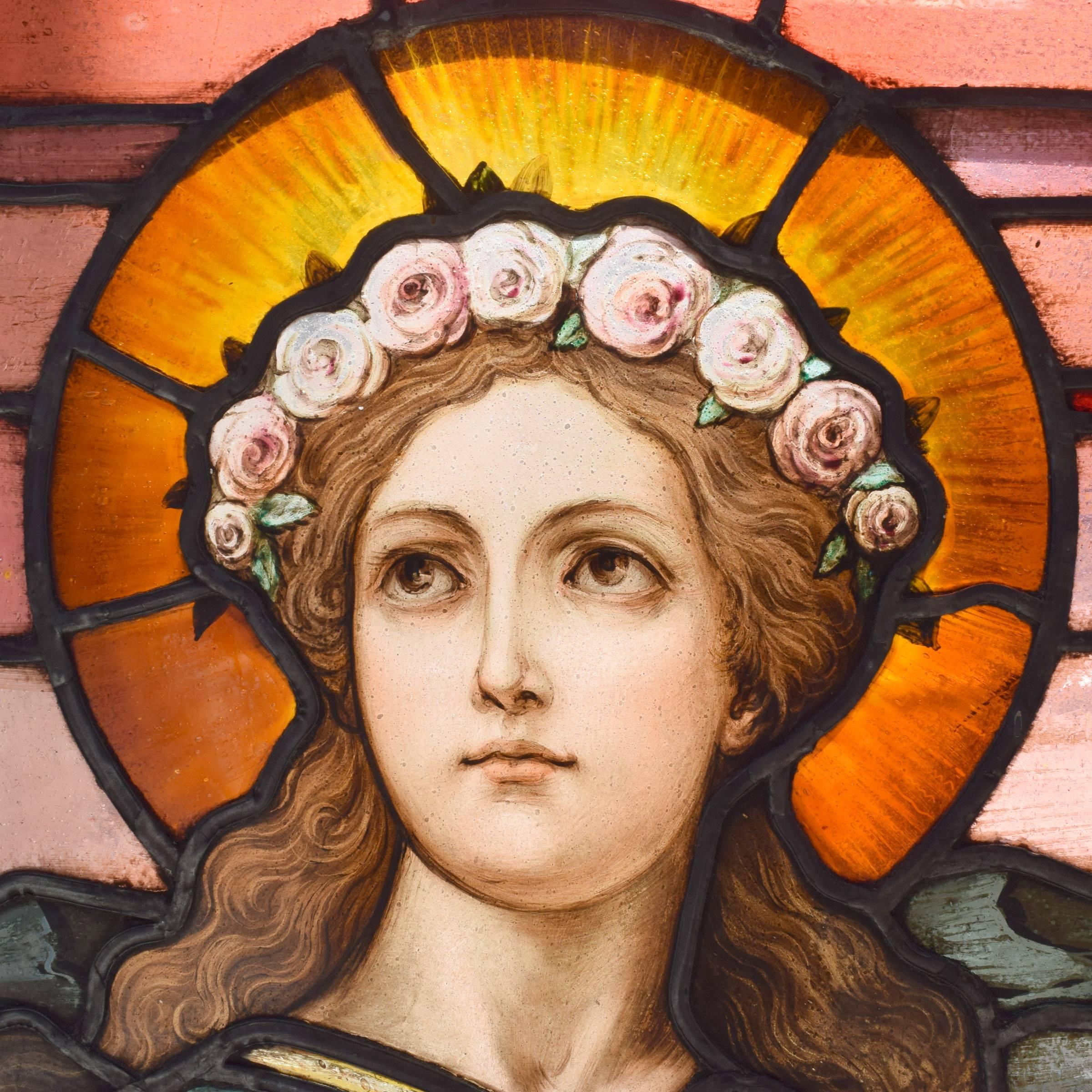 A fantastic art glass scenic arched top window from an American church. The window depicts St. Lucy, the patron saint of the blind, standing under a red sky with a castle in the distance. She’s wearing a crown of roses and grasping a sword with one