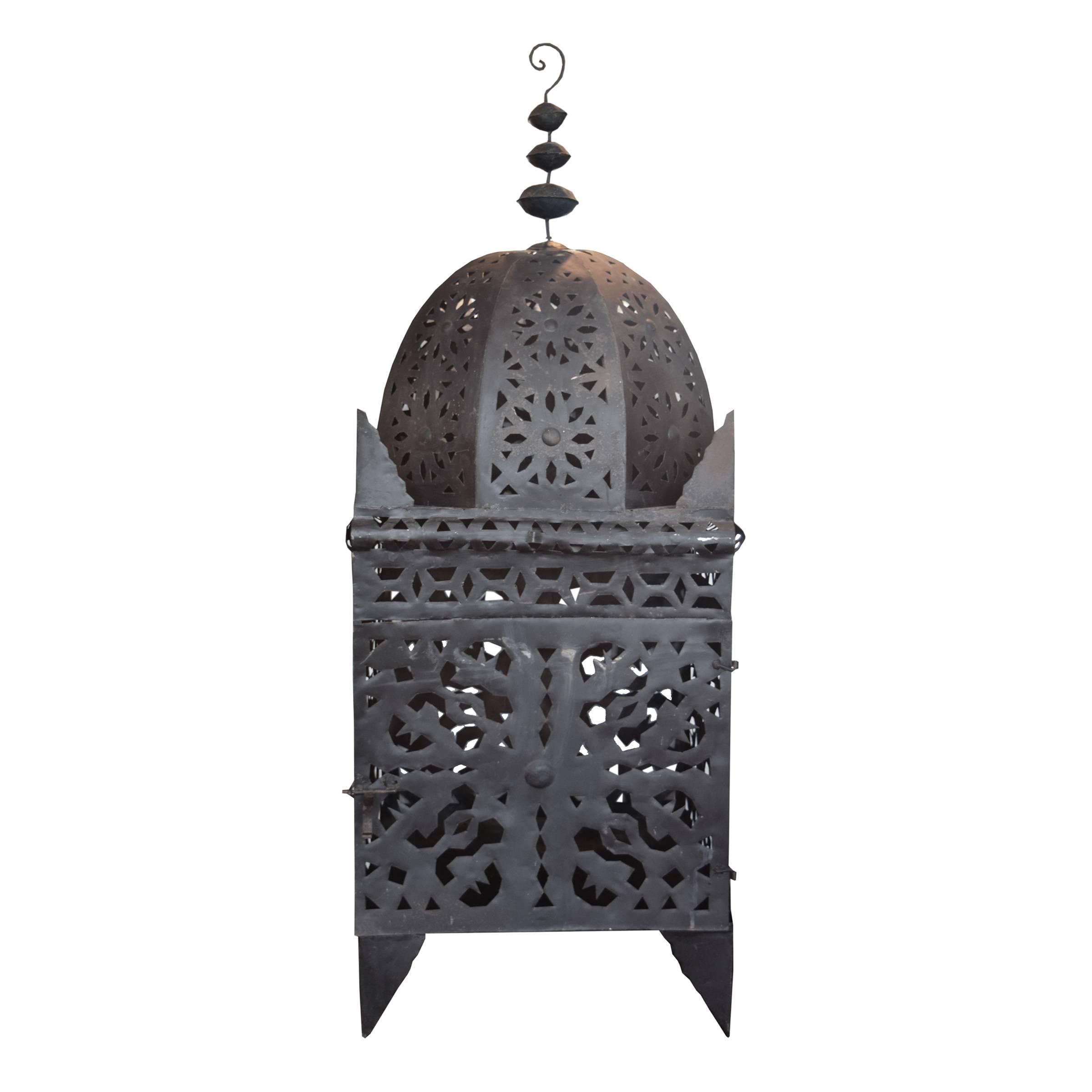 A Moroccan pierced tin Koutoubia style oversize lantern with one hinged door, four legs, intricate pierced detail from top to bottom and a scrolled hook, circa 1960. Two available.