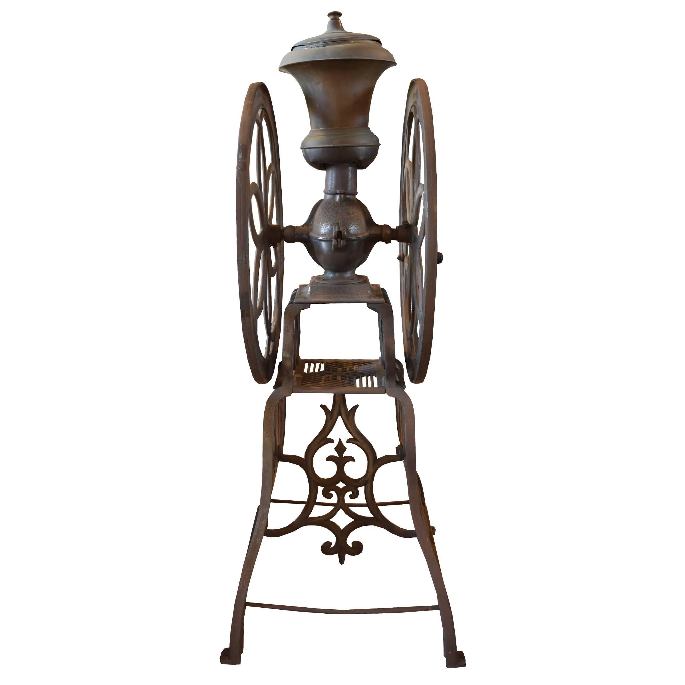 An American cast iron coffee grinder by Enterprise Manufacturing Co. of Philadelphia, Pennsylvania. This unit consists of a lidded funnel, crank wheel with wood handle, floor stand, and patent date marked 