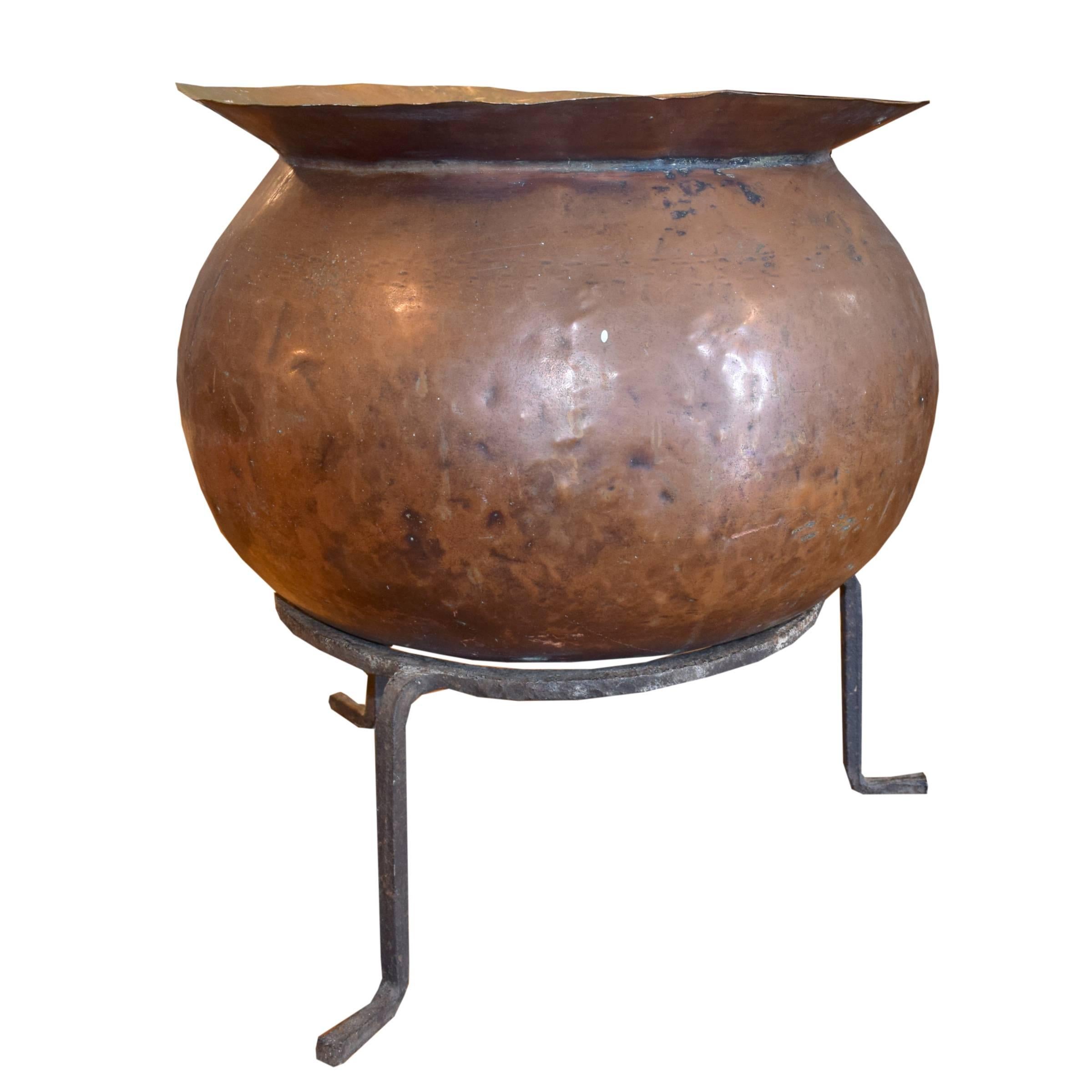 A French copper cooking vessel with a hammered body and a wide lip, on a metal stand, circa 1900.
 