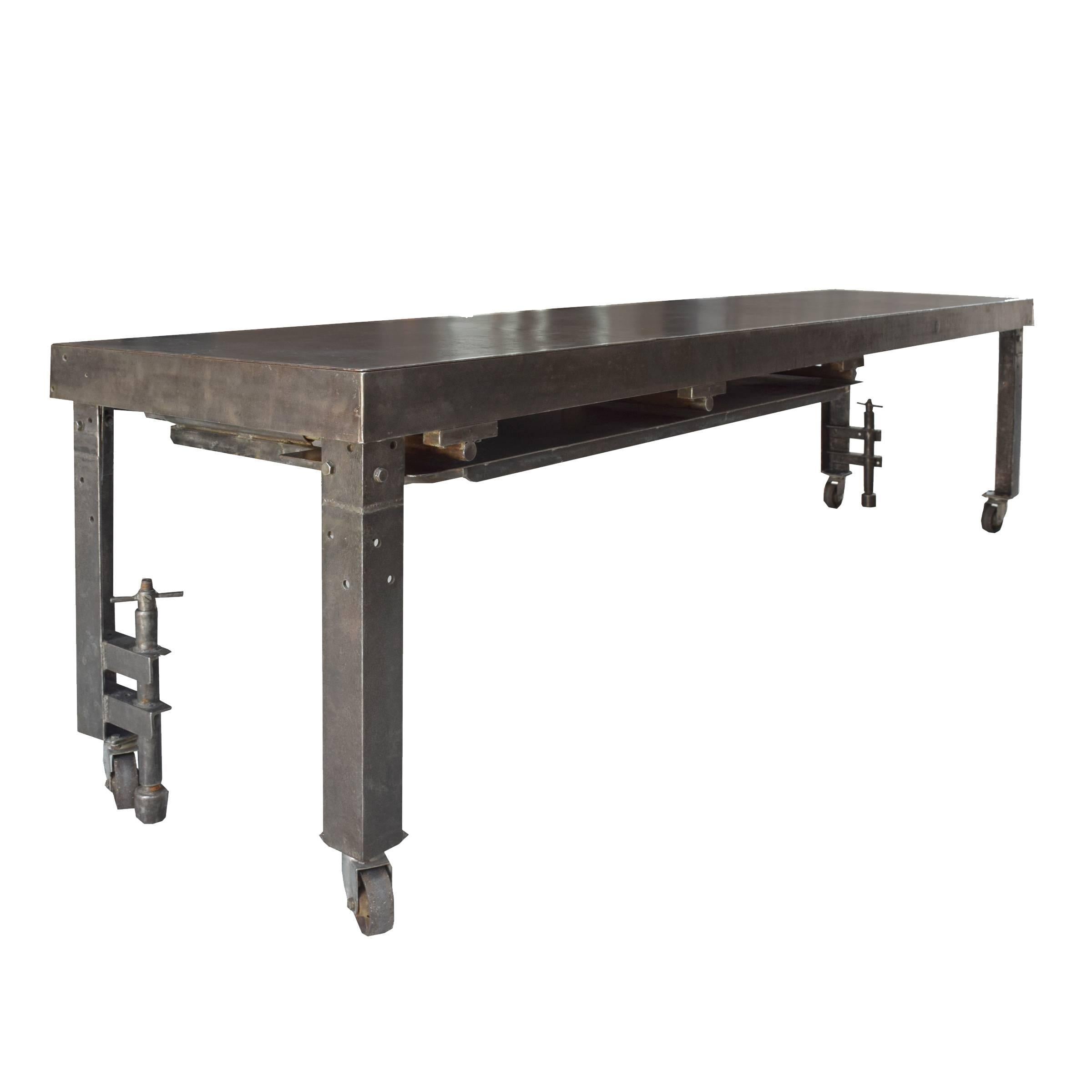 A metal industrial table from a candy factory raised on four legs ending on casters, two of which feature hand crank brakes. The table originally had tubing coils underneath to heat or cool the table top depending on the type of candy, early 20th