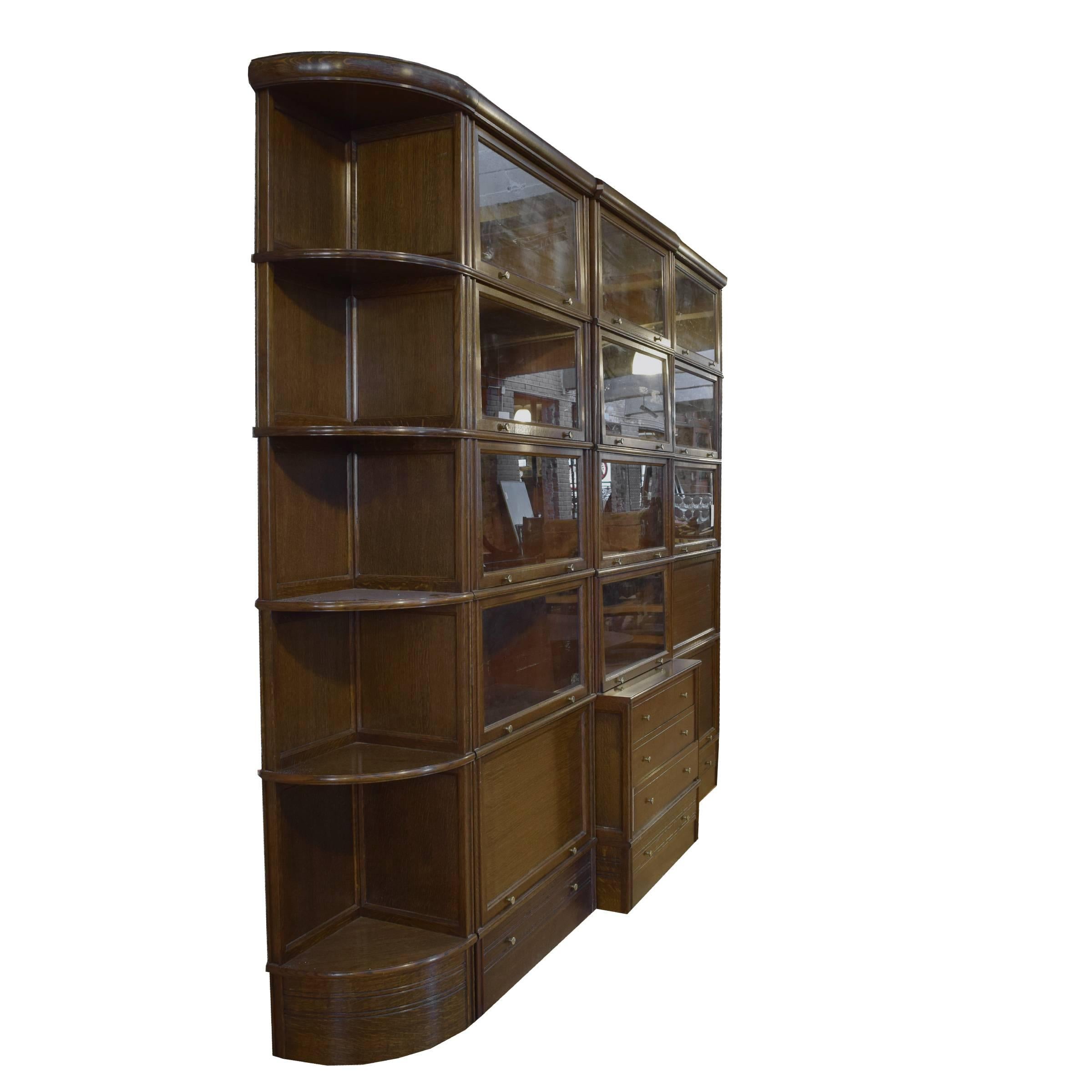 A multi-piece French oak book cabinet with fourteen doors and six-drawer with brass hardware and five shelves. The far right wood door opens into a desk.