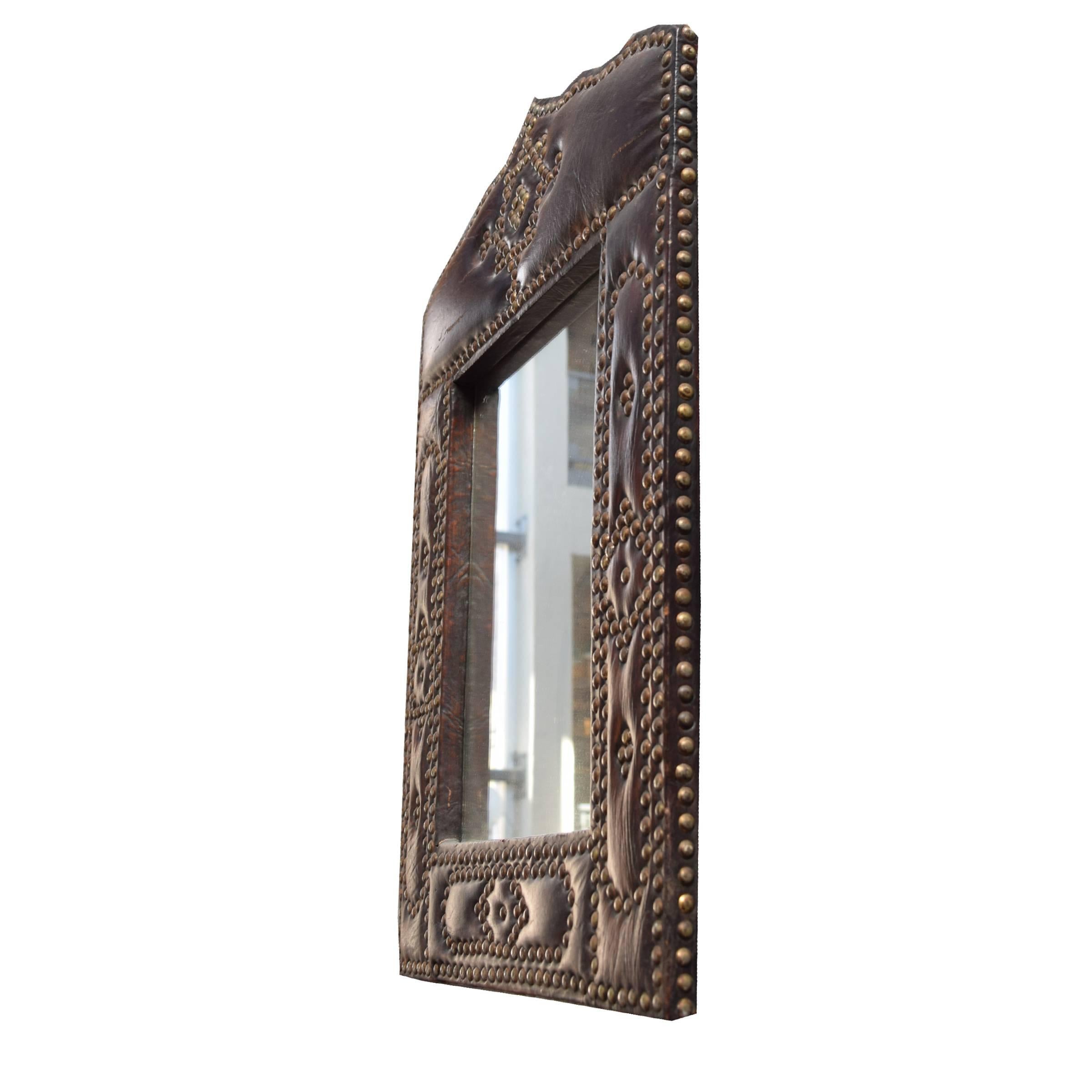 A French mirror with a leather frame and decorative brass nailhead detailing, circa 1930.