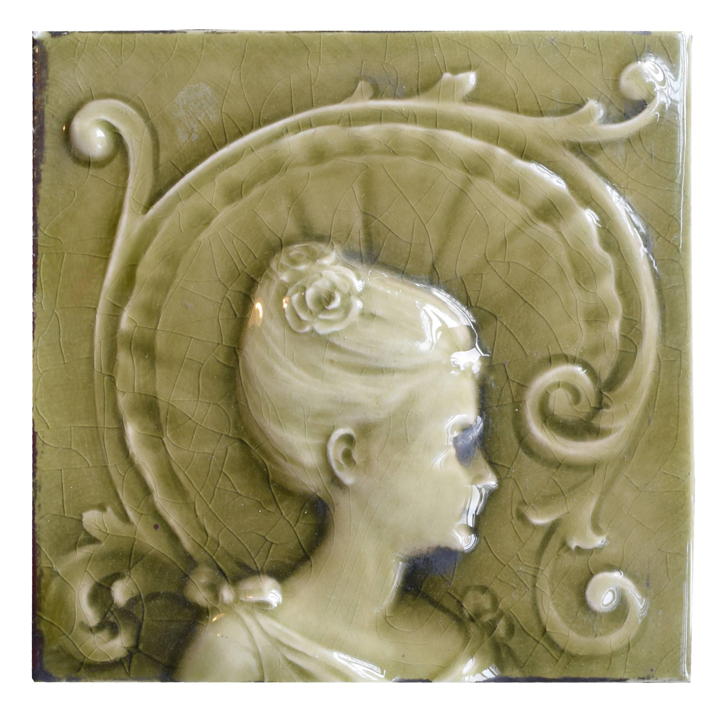 A fabulous three-piece glazed tile set depicting a woman in 18th century costume in low relief by the American Encaustic Tiling of Zanesville, OH. Stamped “A.E. Tile Co. Limited”, late 19th century. The American Encaustic Tiling (1875-1935) was, at