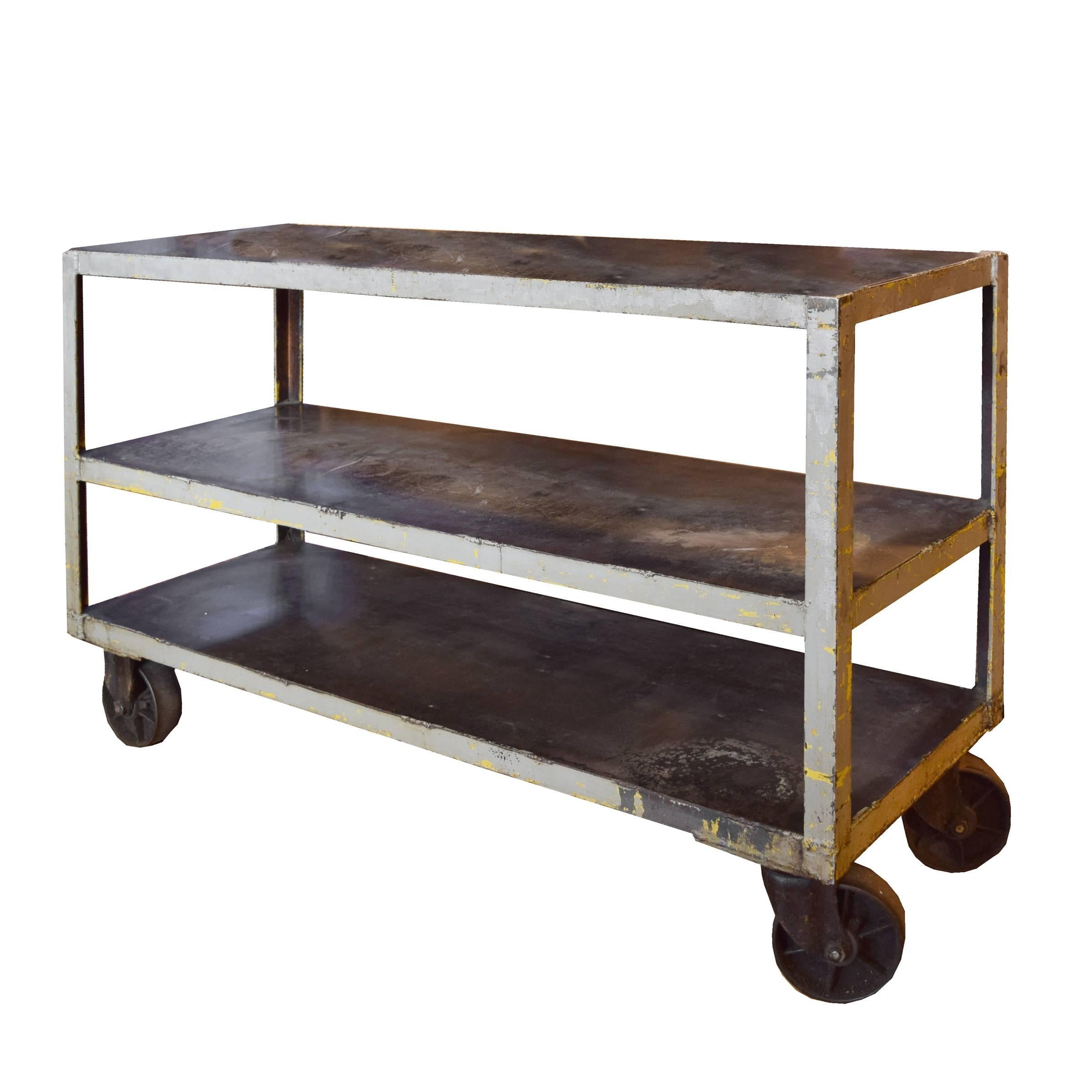 An American Industrial cart with three shelves, on large wheels.  
 