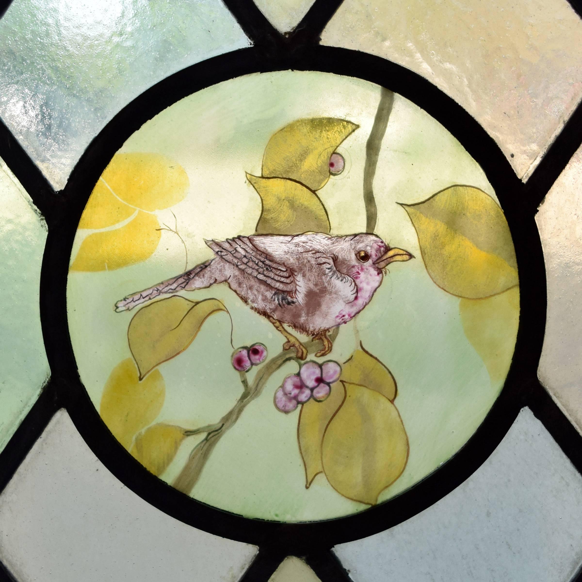 An English art glass window with a colorful diamond pattern and a central medallion depicting a bird on a branch.
