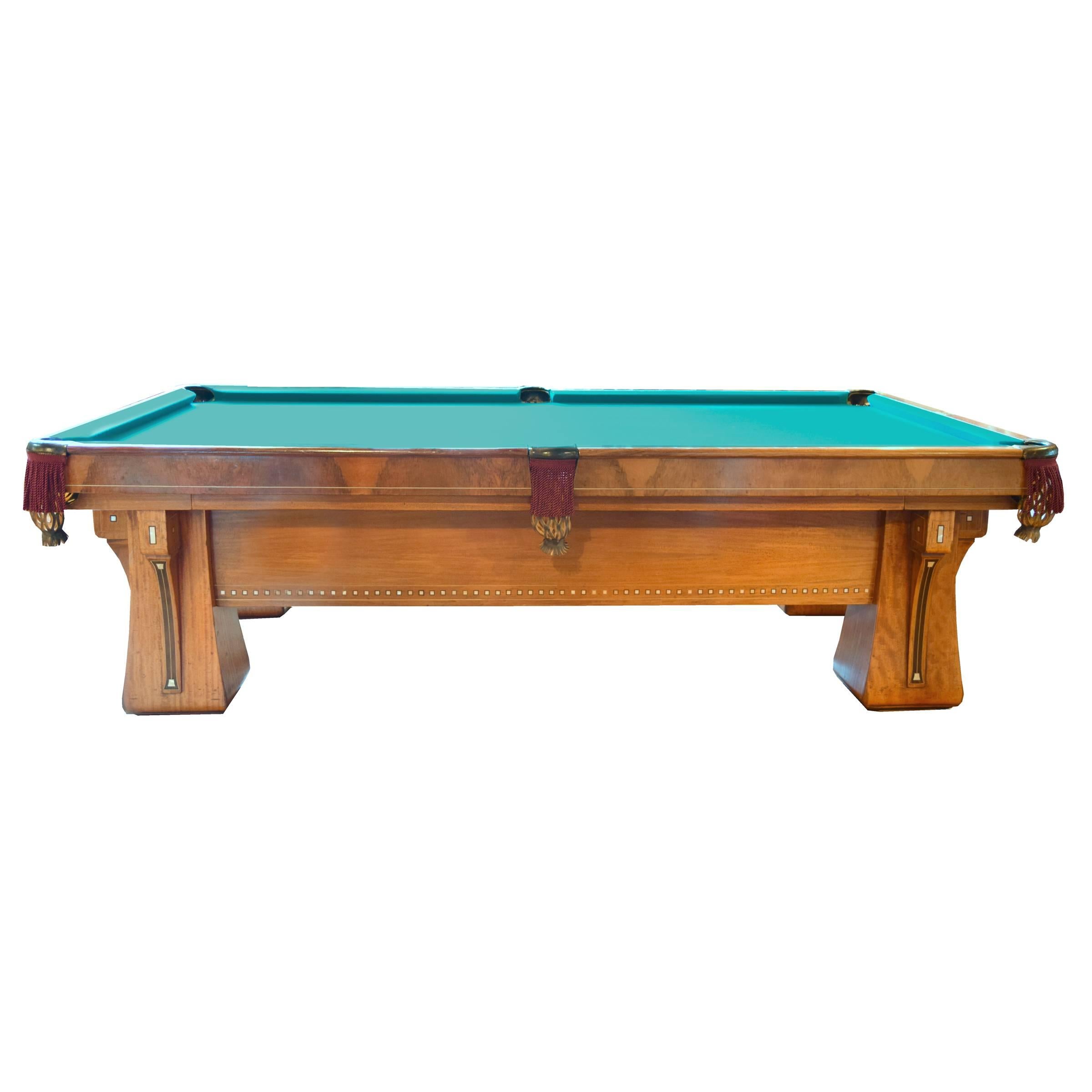An impressive Brunswick Balke Collender Arcade 9 foot pool table in excellent condition with bookmatched burl trim, pearl inlays, and webbed leather pockets, circa 1920. Accompanying this table is a Brunswick bench, balls with wood rack, six cue