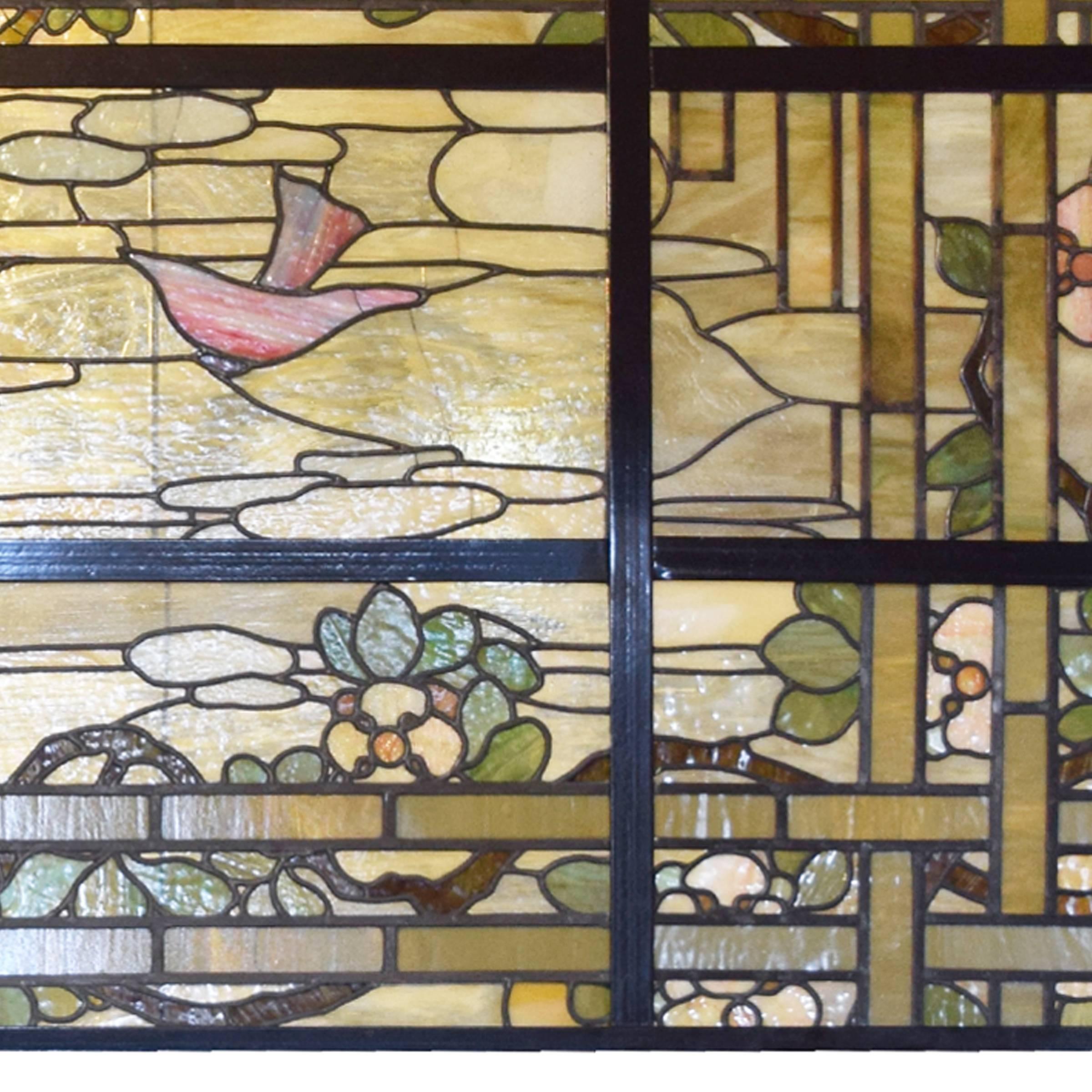 A fantastic extra-large American scenic stained glass window depicting flowers on a trellis and two pink birds flying amongst clouds, circa 1910.
