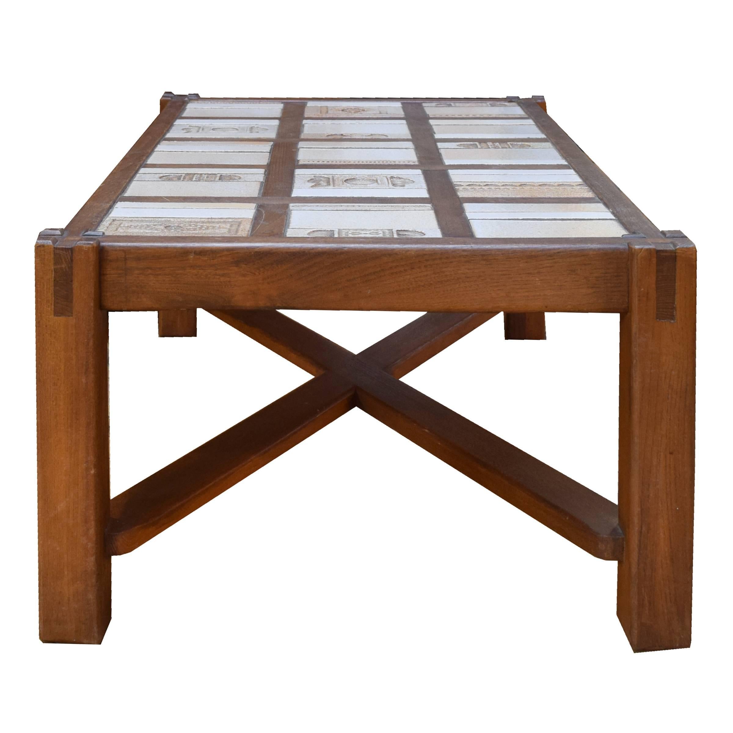 A great mid-century wood coffee table with crossed stretchers and a tile top with stamped geometric and floral patterns.