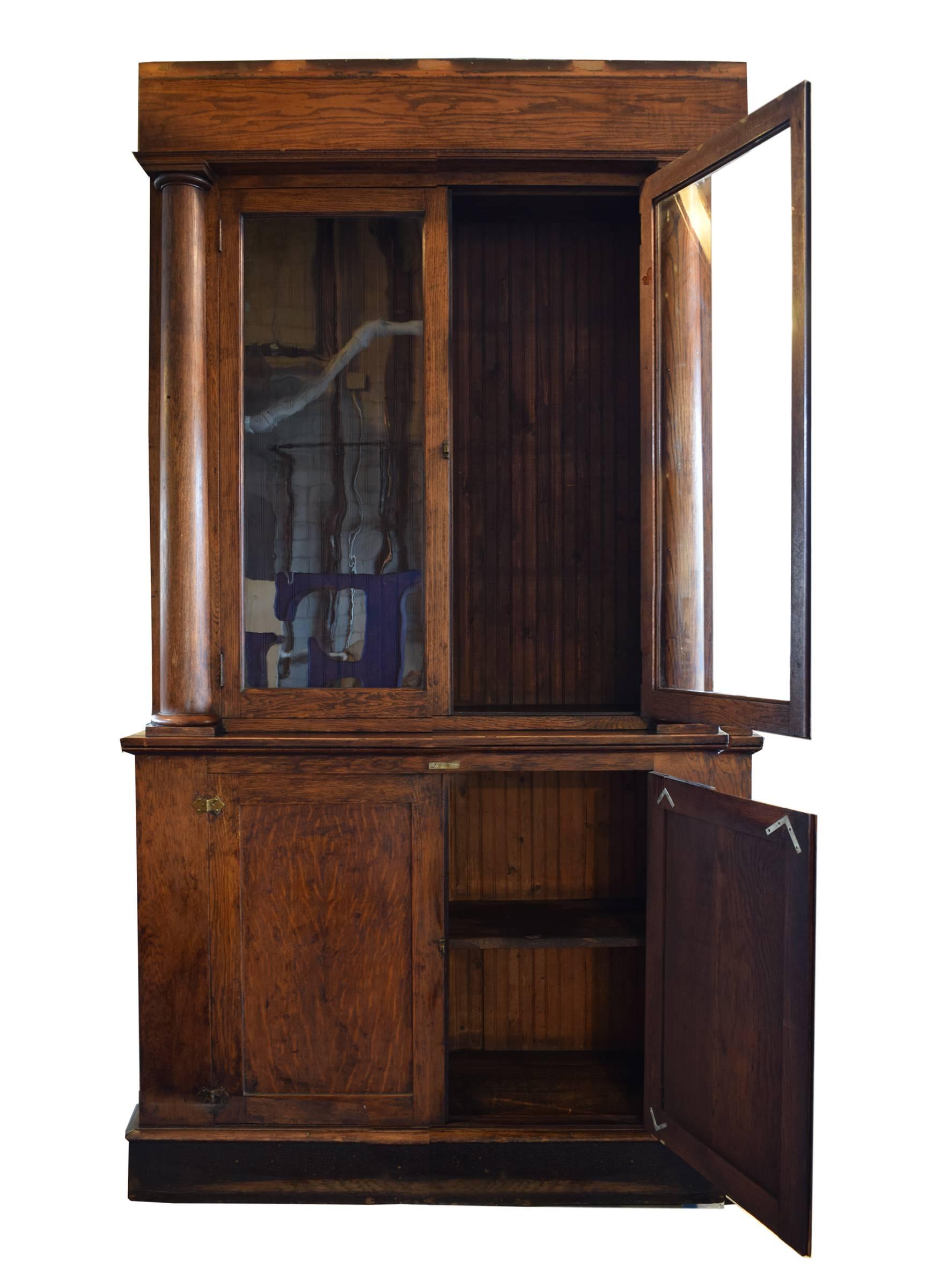 An American oak liquor cabinet by Brunswick furniture from a Chicago saloon. The cabinet features two top doors with original glass and two lower oak doors that open to a deep storage space with a shelf. Details include pillars and brass hardware.