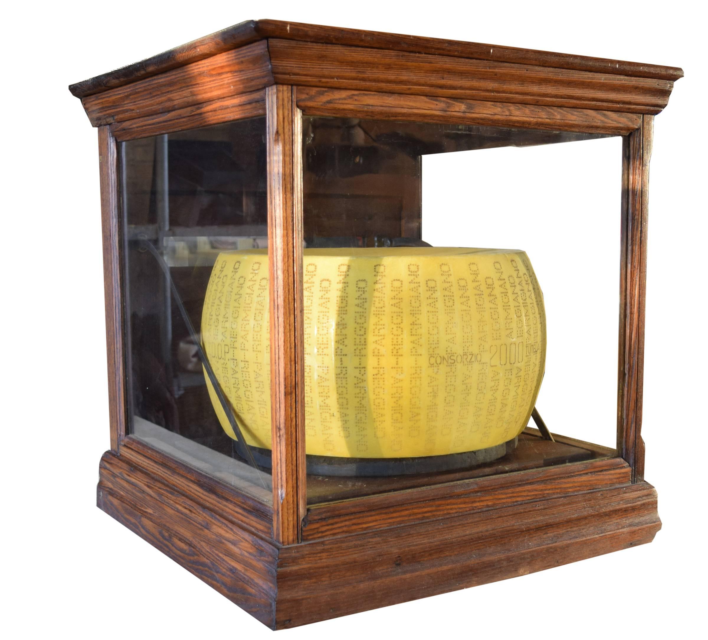 An early 20th century American oak cheesemonger's display case with sliding platform mechanism. Three sides are glass and the fourth is wood with a screened vent. When the back door is opened, the cheese simultaneously slides out from the case.