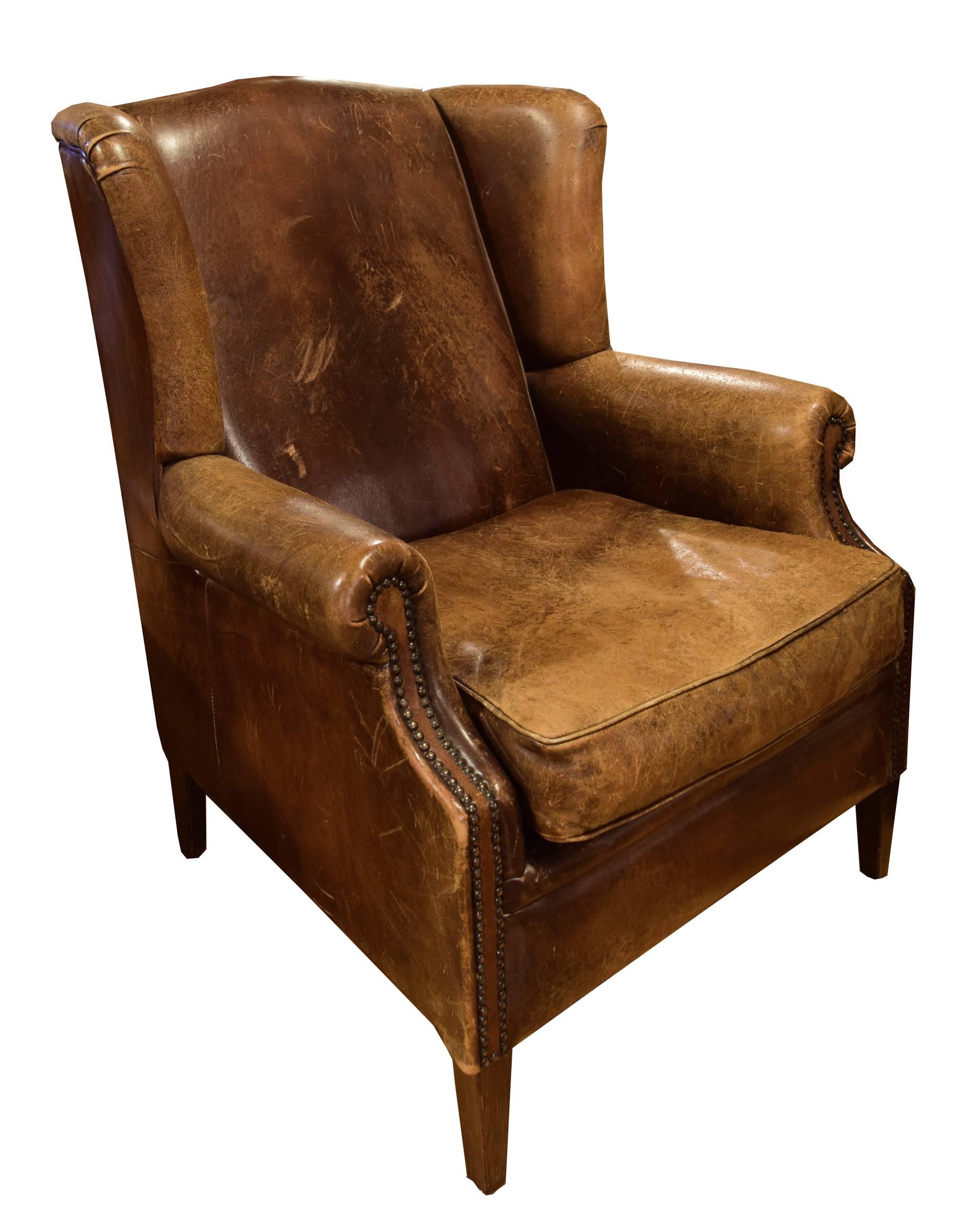 A fabulous Italian leather wingback chair from the early 20th century. This chair has wooden feet, scrolled arms with studded detailing, and a beautiful patina.