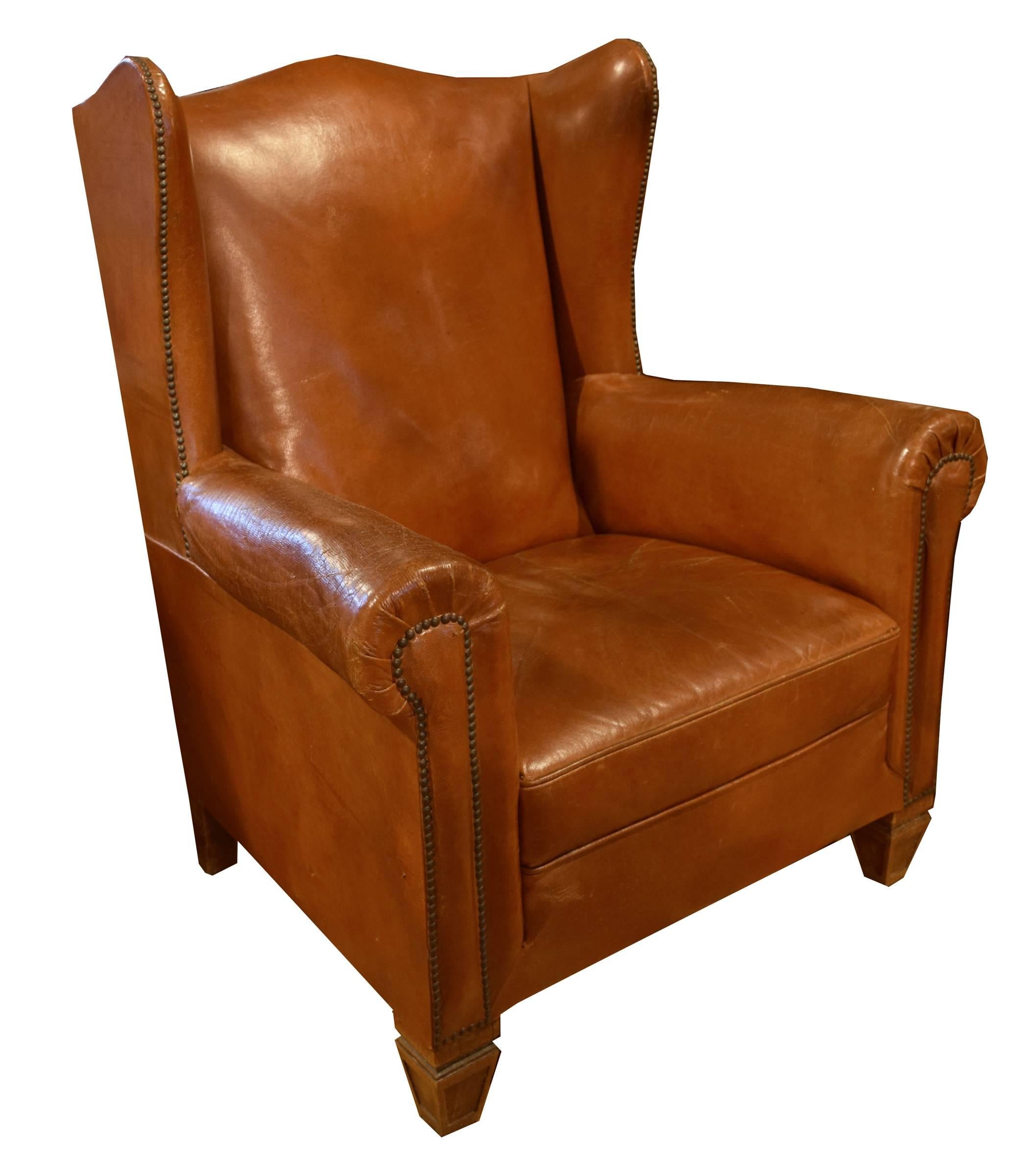 A cognac colored leather wingback chair. This leather chair has nice geometric feet and gently curved arms with studded detailing.