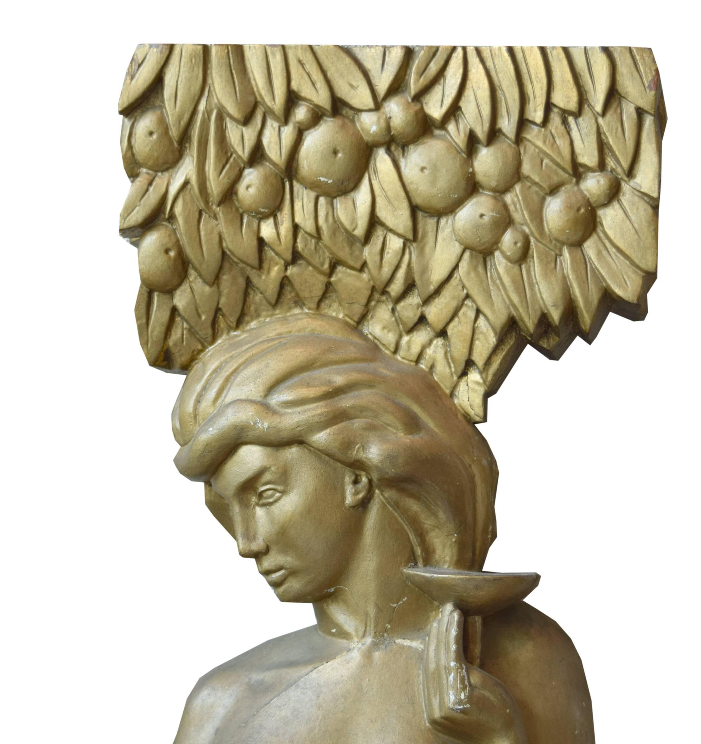 An American carved wood and gilt painted Art Deco maiden. The maiden, standing beneath a fruit tree, holds a wine glass in her left hand and fruit in her right hand. A fawn hides behind her.
