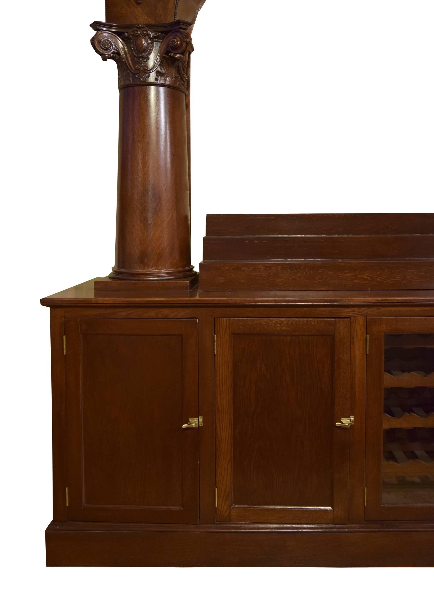 A newly refinished 19th century American oak back bar with intricately carved Corinthian columns supporting an arched top with floral carved details. The bar is complete with two bottle risers, five drawers, and eight doors. Four doors are glass