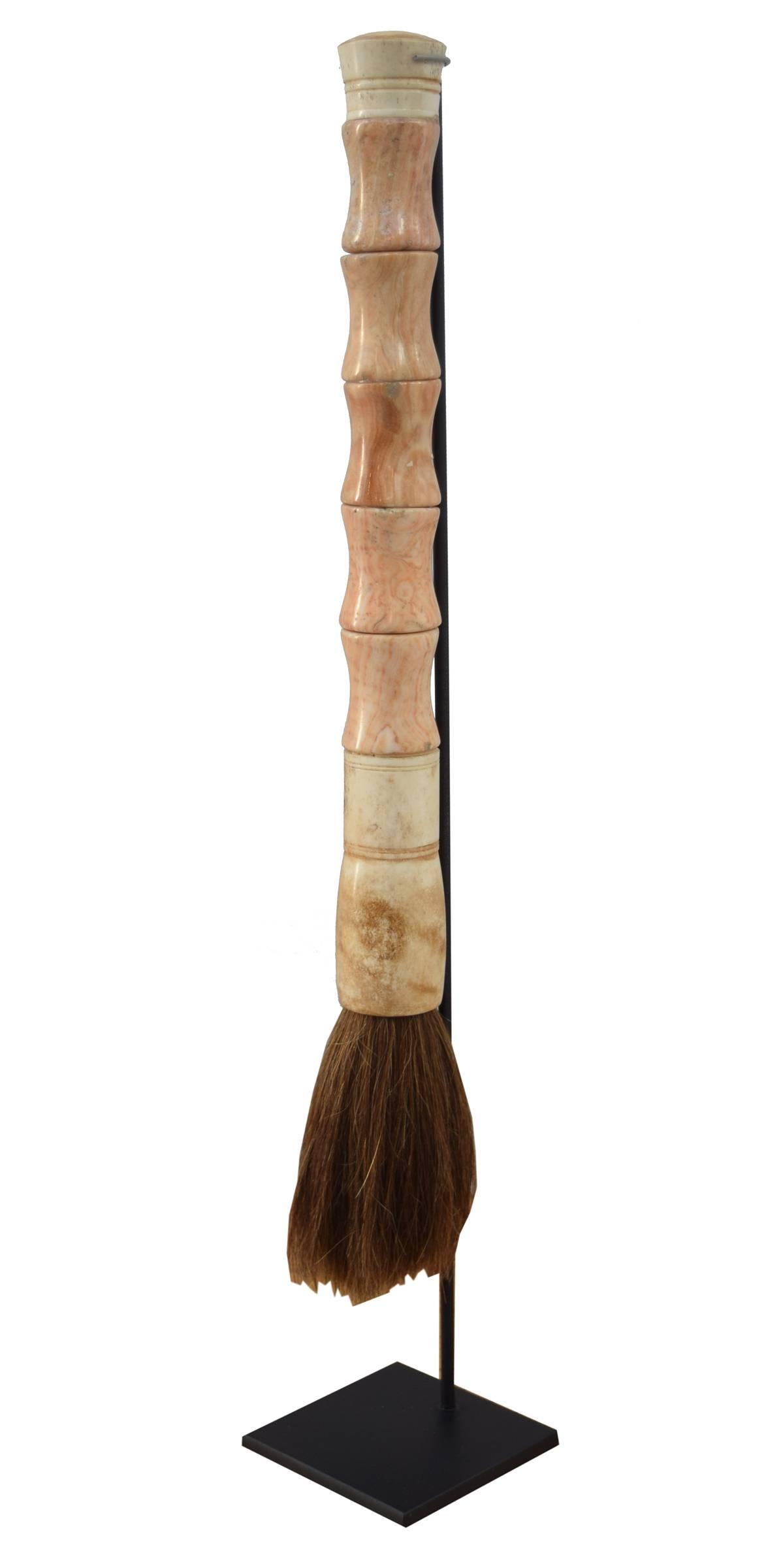 A Chinese calligraphy brush with pink-toned ribbed agate handle on a custom stand.