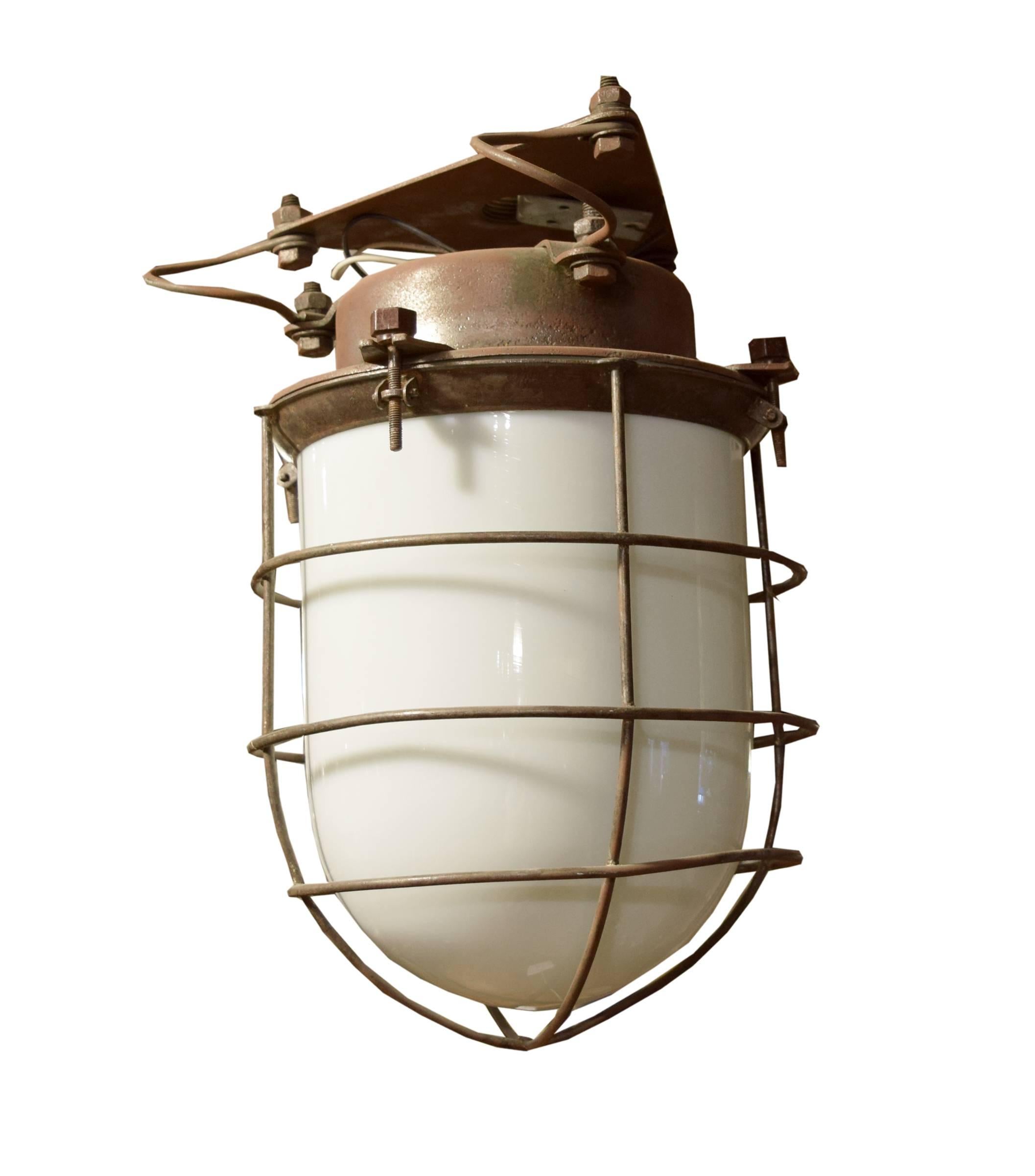 A fantastic Argentine explosion proof light fixture with an iron body and cage on spring mount with opaque glass shade. c. 1940's. Three available.