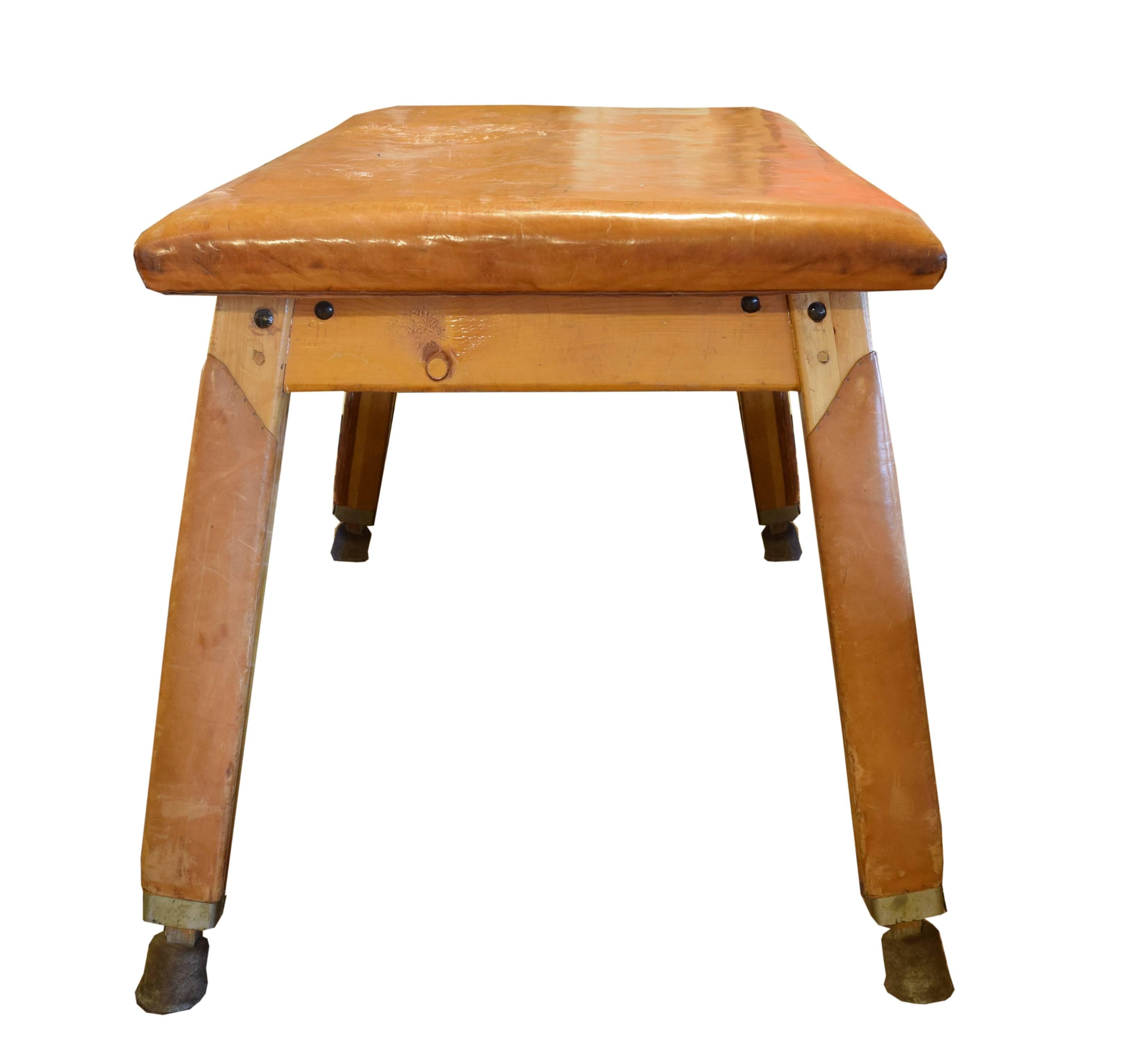 A vintage wood and leather vaulting table with a wide leather top and tall tapered square legs and a great patina, from a gymnasium in the Czech Republic, circa 1930.