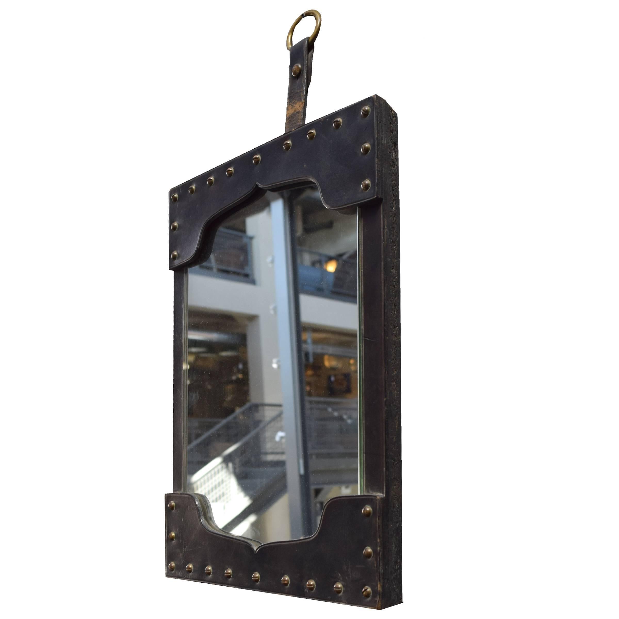 A French Mid-Century mirror with a leather frame with brass nailhead trim, hung by a leather strap with a brass ring.
    