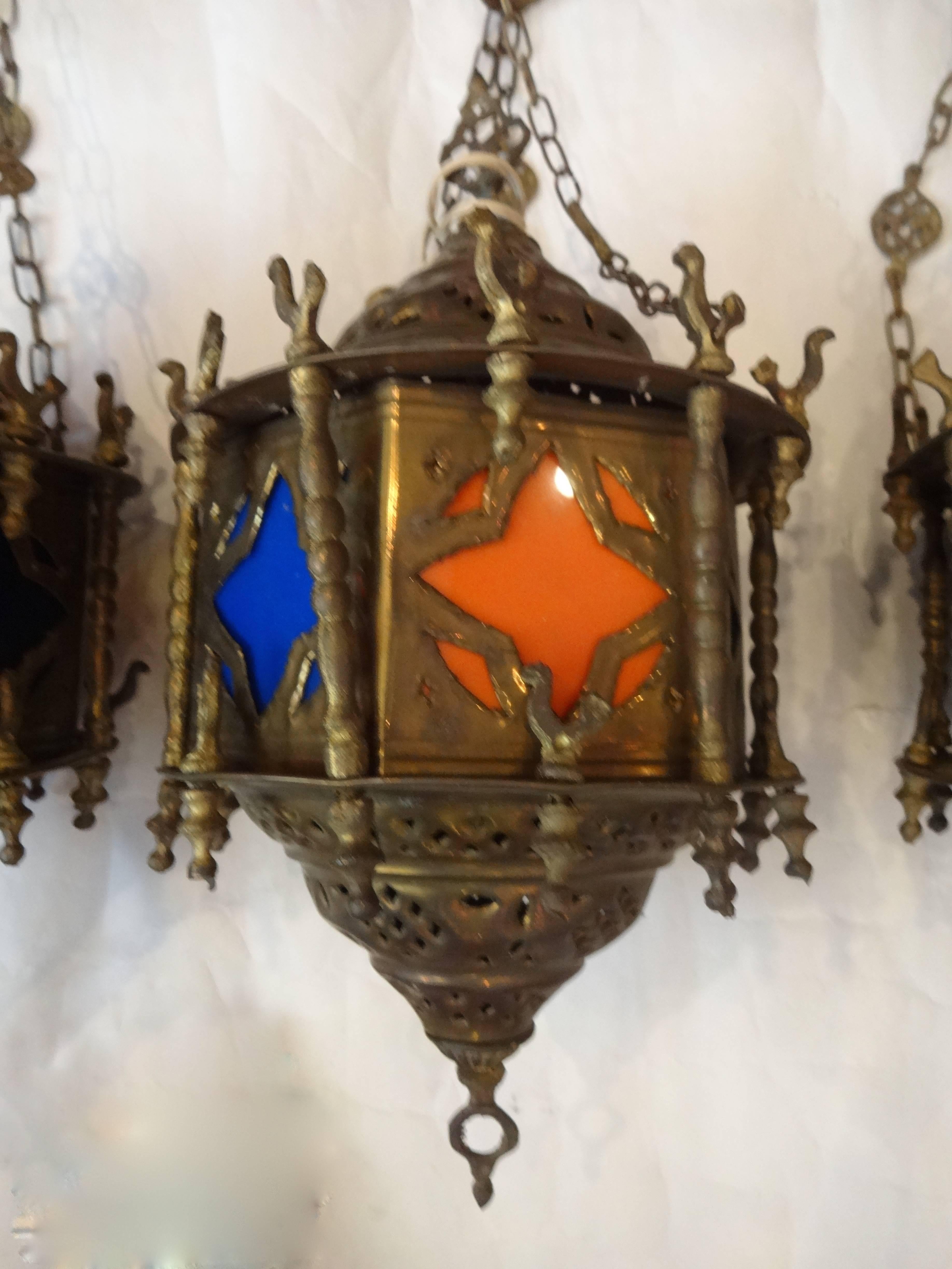 A set of three Moroccan brass and glass hanging lanterns with decorative chains. All three are the same size, slightly different designs. Originally were lit with candles, later electrified. Can be purchased separately ($950.00 each.).