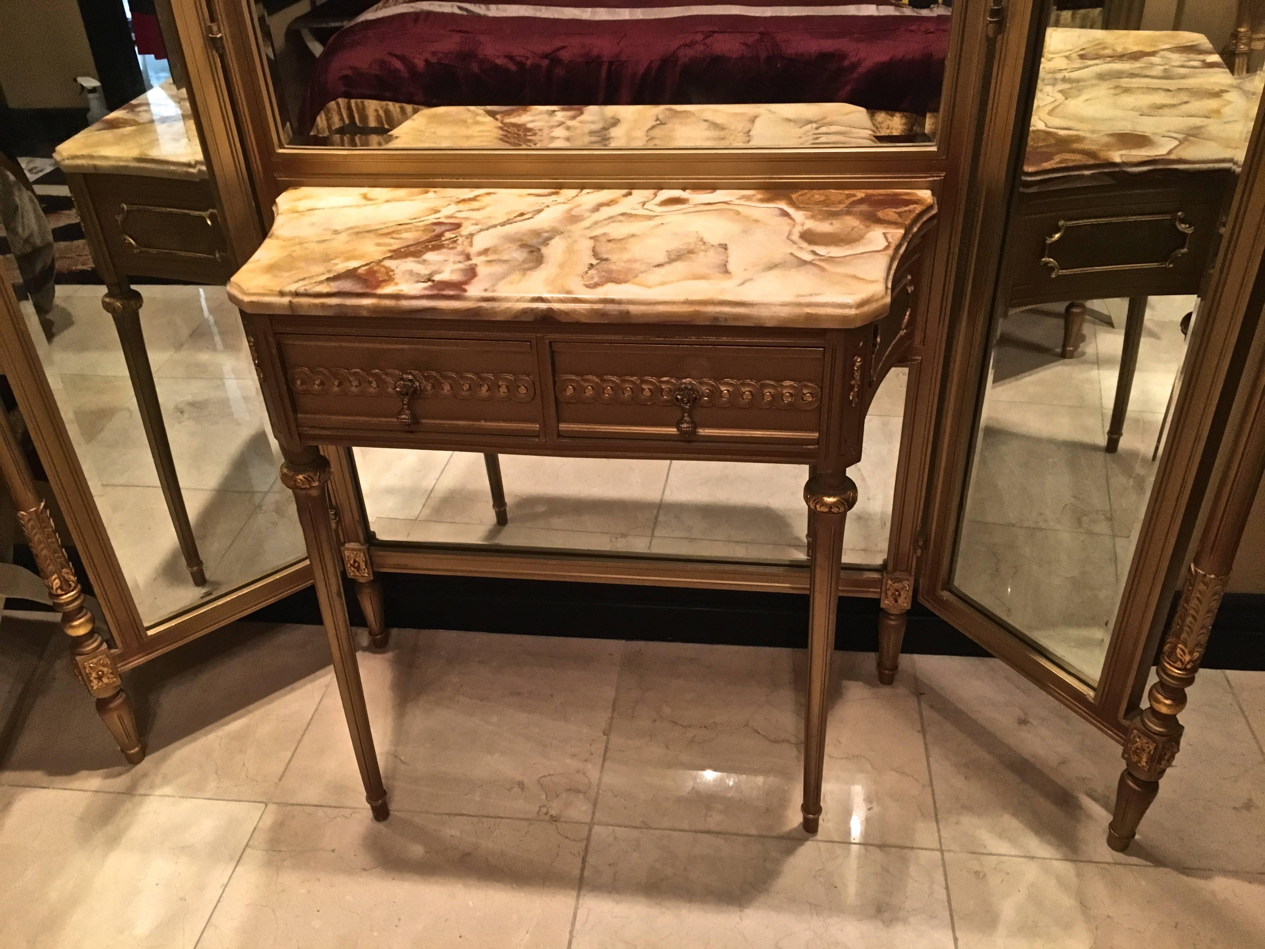 A hand-carved giltwood Louis XVI style tri-fold beveled vanity mirror with dressing table. The dressing table has a beautiful onyx top and two drawers.