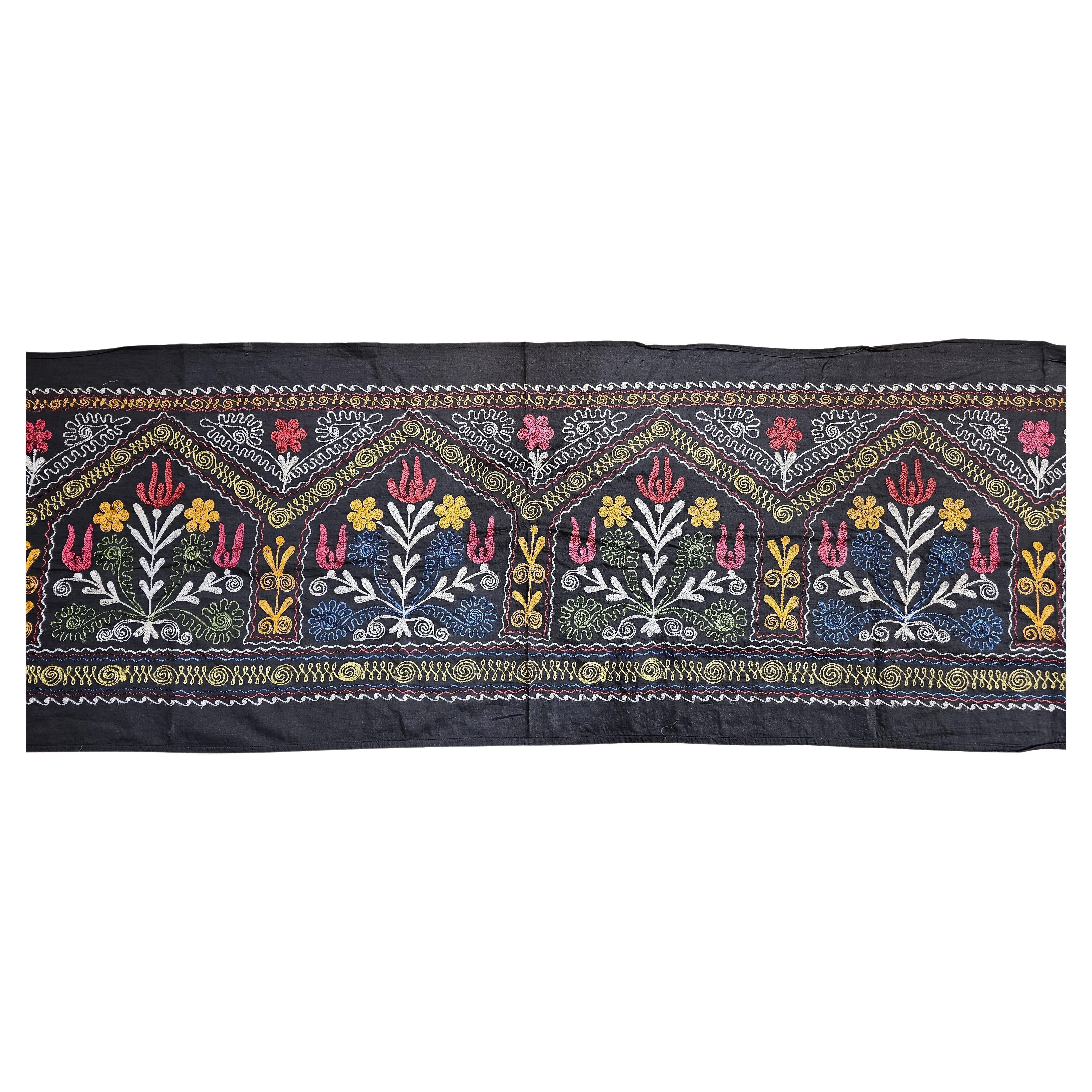 Vintage hand-crafted Suzani silk embroidery from Uzbekistan in Central Asia in black cotton background and designs in silk in black, blue, green, ivory, yellow, and red.  The design of each panel consists of finely silk embroidered floral patterns