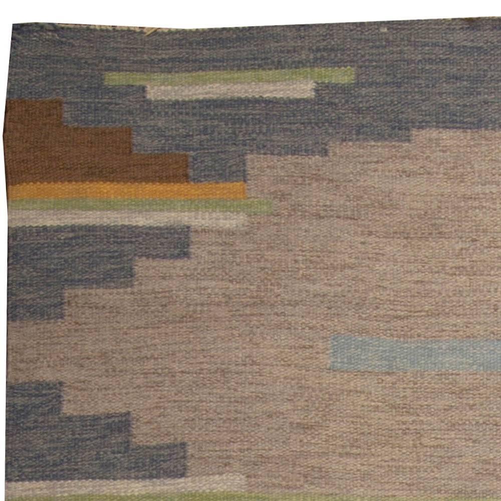 A vintage Swedish flat-weave rug signed AB in the lower right corner. Alternating Bands of grey and taupe create the back round defined by blue, green and ivory stripes.