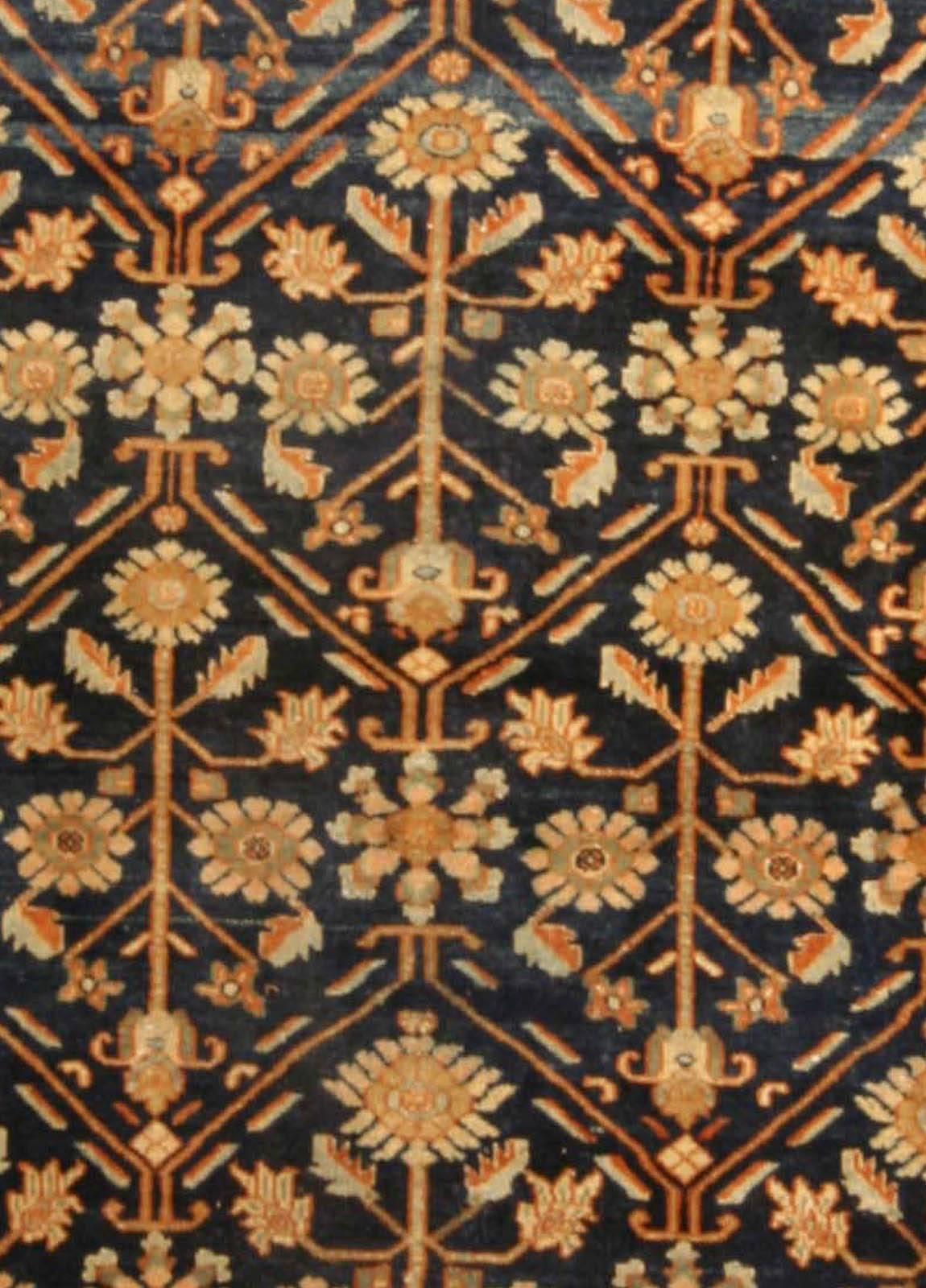 An early 20th century, Persian Heriz carpet, the midnight blue field with a restrained spacious trellis overall of angular floral vinery and palmettes within a peach stylized vinery and palmette border.