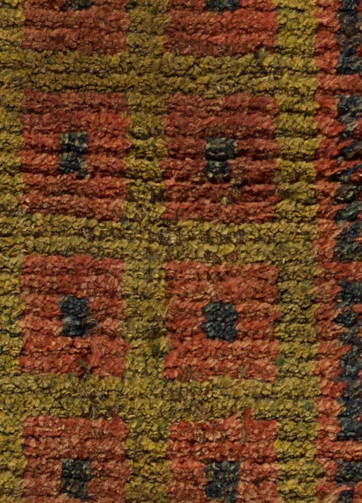 This antique Tibetan monastic runner features an all-over design of geometric motifs in earthy shades of red and green, with a pile border in black, circa 1920. The richly saturated colors make the antique runner carpet an intriguing piece of home