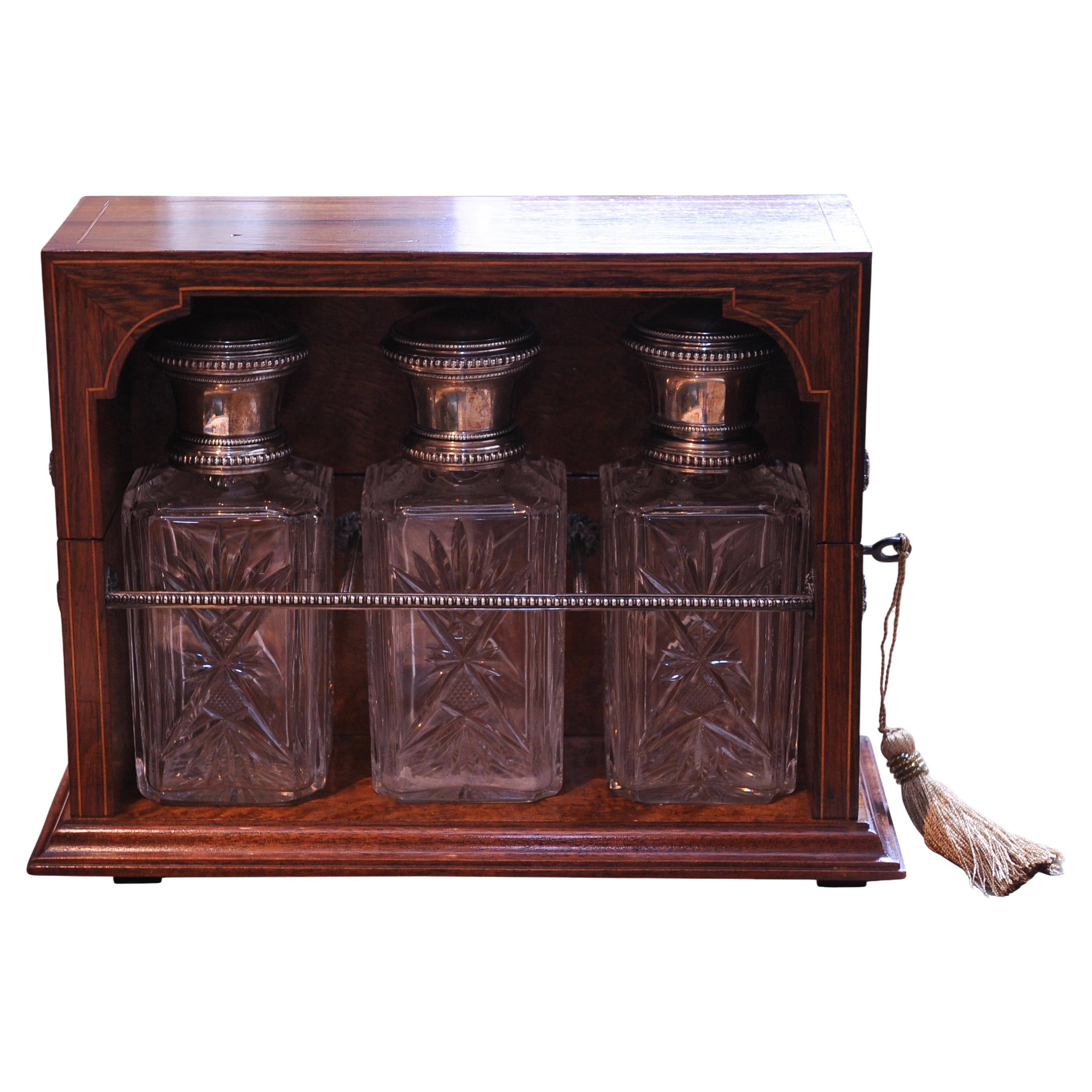 A Beautiful 19th century Continental Rosewood and Amboyna Inlaid Tantalus revealing three cut glass decanters with silver trims & lids.

Decanters Are Revealed Inside Via a Silver-Plate on Brass Piano Hinge With Side Decorative Cast Roundels &