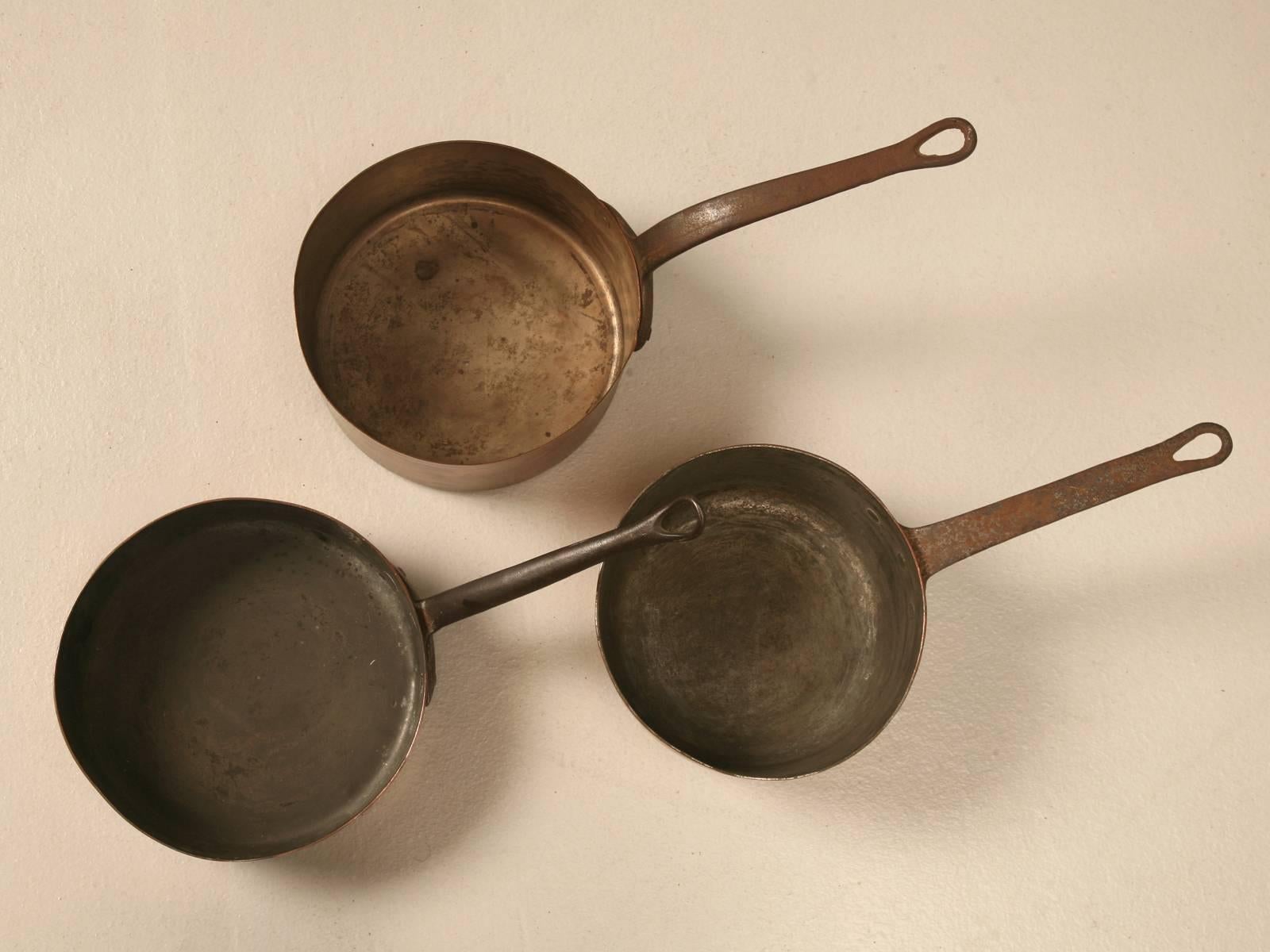 Set of three antique French copper pots and pans from the early 1800s to the mid-1800s, would be my best hypothesis on the age. Wonderful to decorate a country style kitchen, as we have done ourselves by hanging them from an old meat rack over the